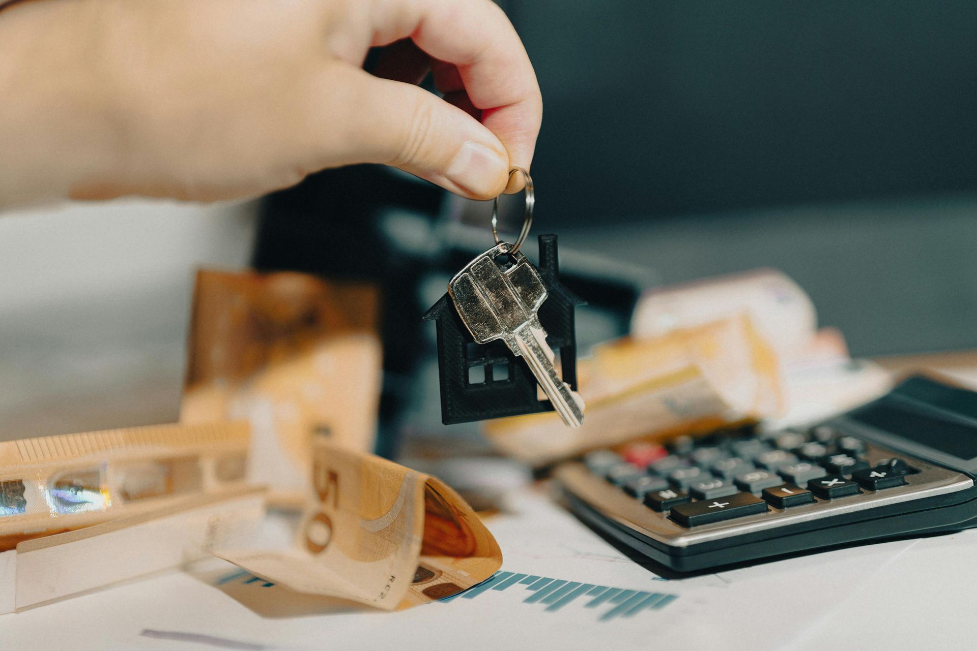Hand holding house key over cash, calculator, and financial documents. Property and Cash Seizures (DEA and Local) Law Attorney in Nashville, Tennessee