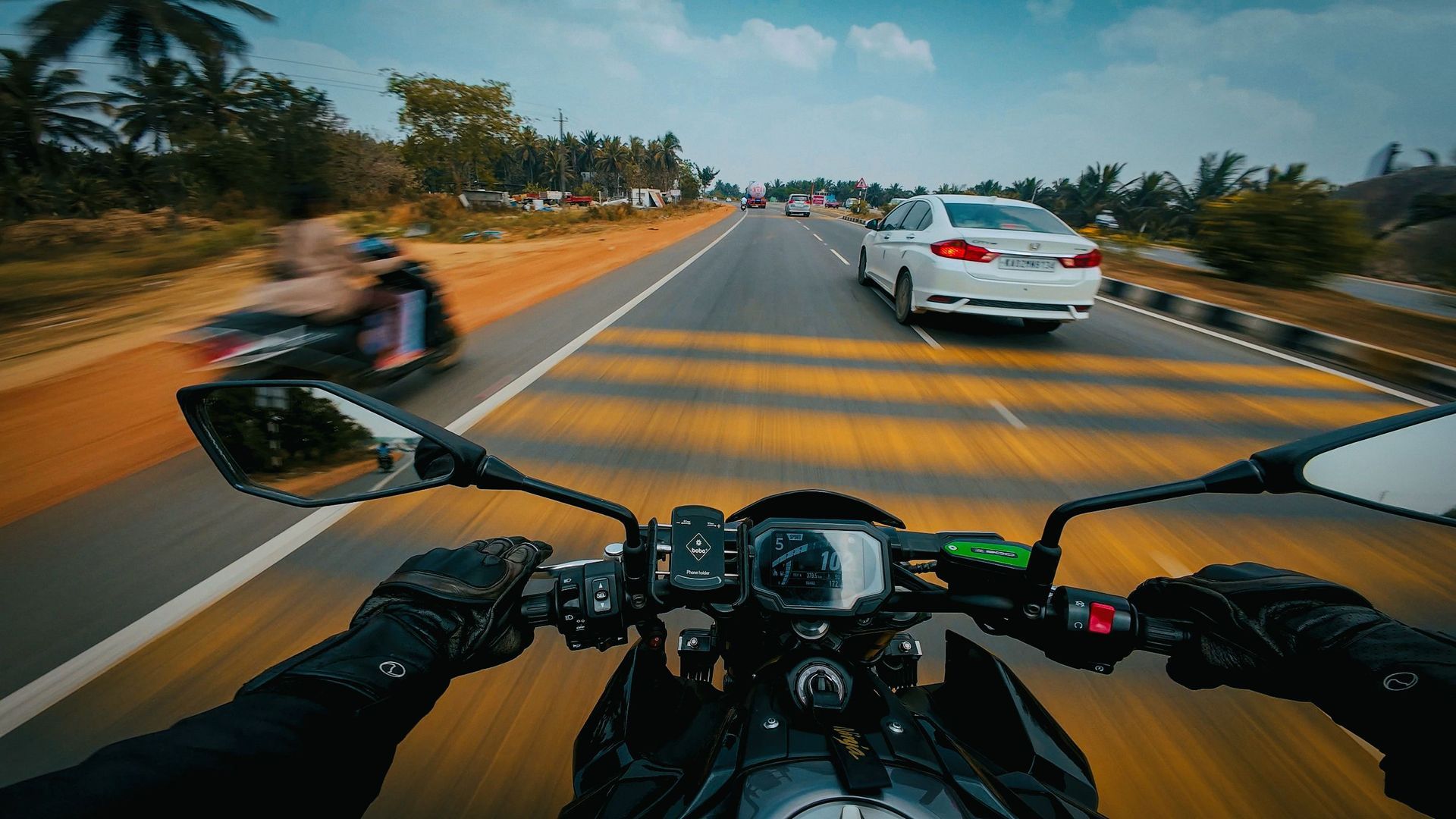 A view of a motorcycle dashboard with a street and a car in the background