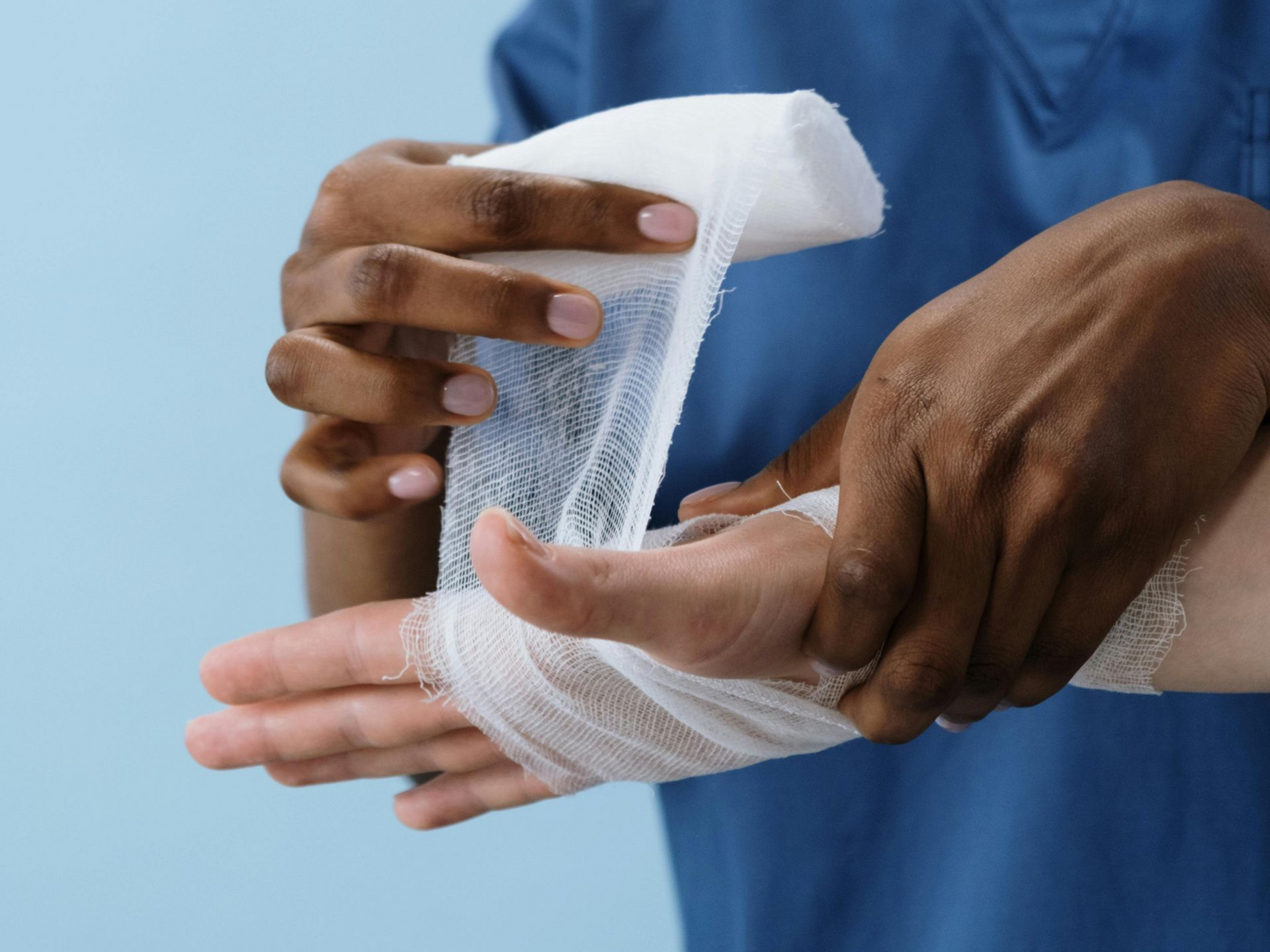 Dark-skinned person bandaging a light-skinned hand with white gauze bandage against a blue background. Personal Injury Law Attorney in Nashville, Tennessee