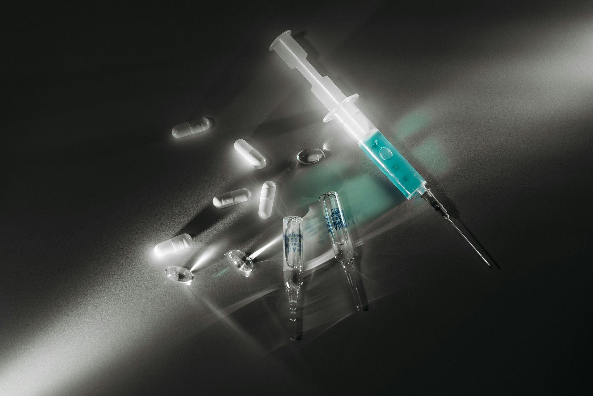 Syringe with blue liquid, pills, and vials on a dark surface, lit from above. Drug Paraphernalia Law Attorney in Nashville, Tennessee