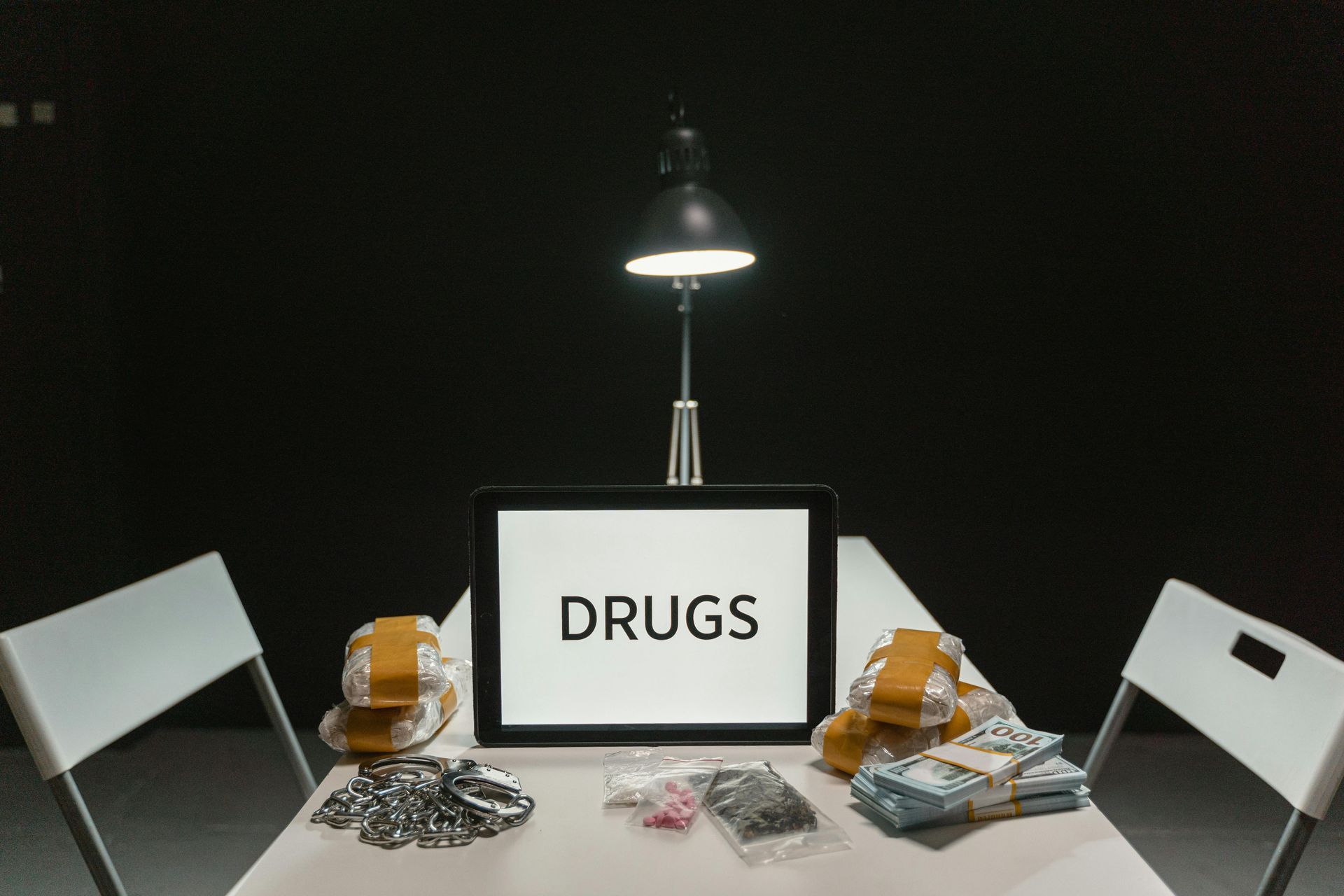 Table with drugs and cash under a lamp; tablet says