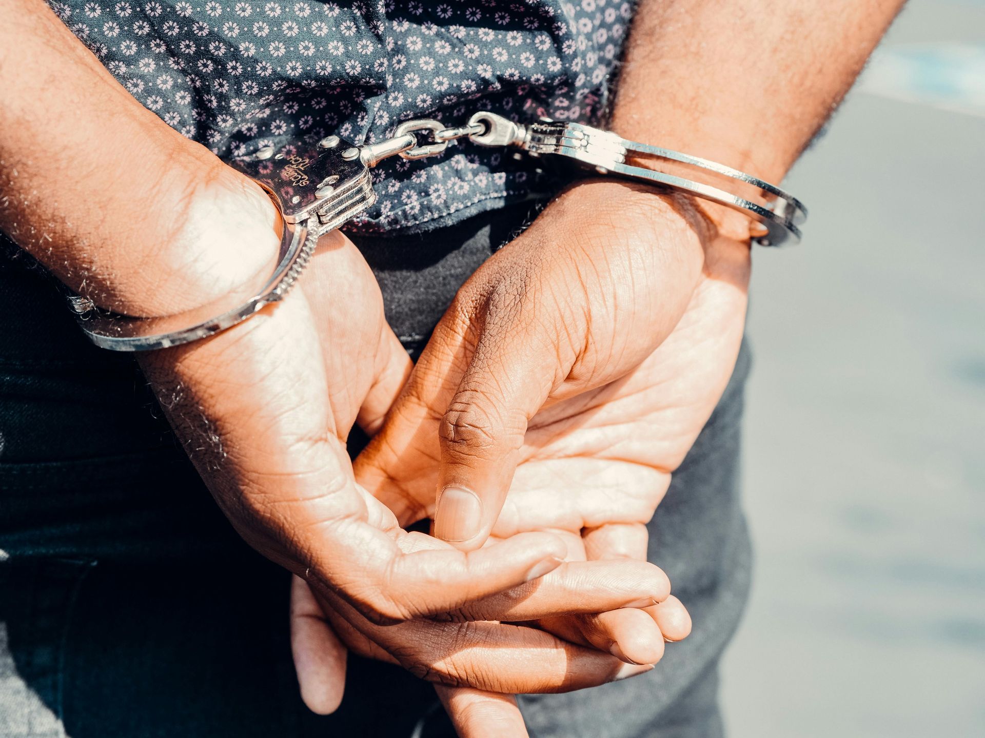Person's hands cuffed behind their back. Silver handcuffs, dark shirt, partial view. OP Violations Law Attorney in Nashville, Tennessee