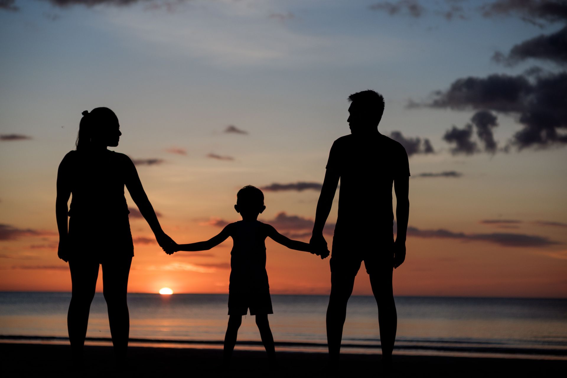 Two parents holding their young child’s hands, with the child standing between them