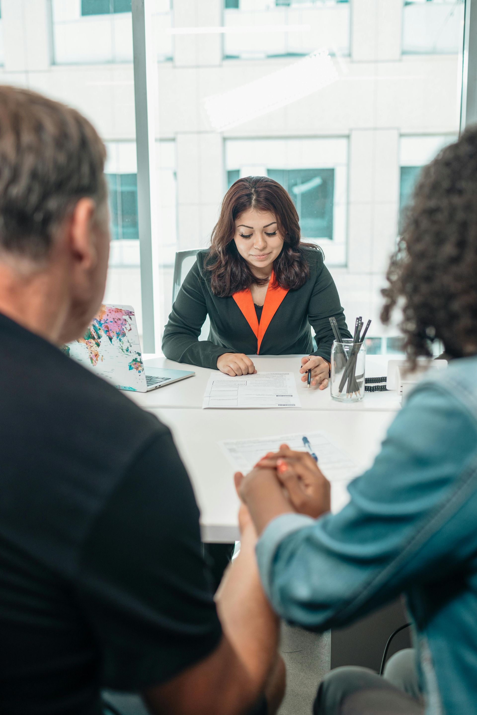 Woman in suit at desk with couple holding hands. Office setting with large windows. Post-Divorce Law Attorney Matters in Nashville, Tennessee