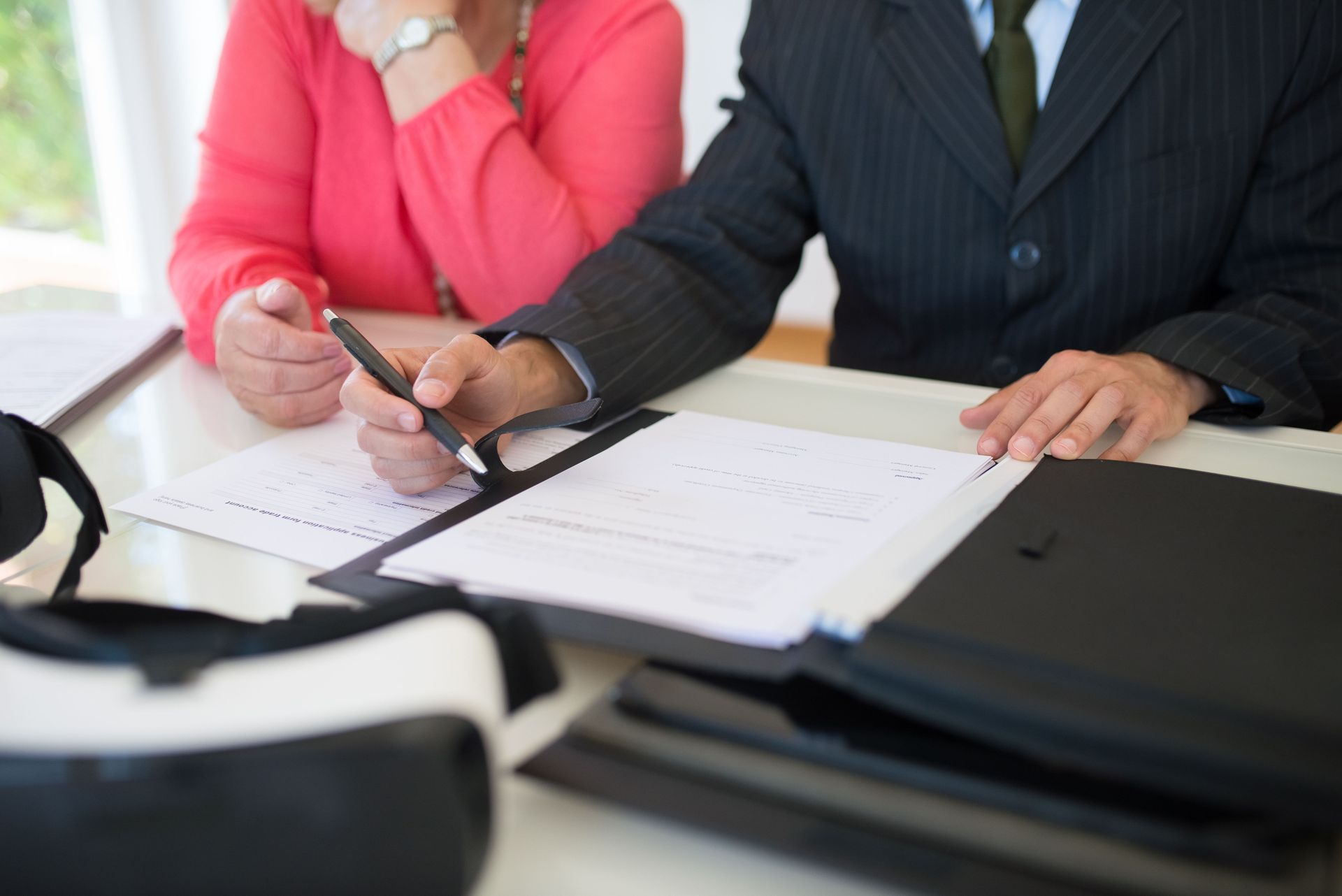 A woman signs a legal document at a table while a man in a suit reviews the paperwork beside her