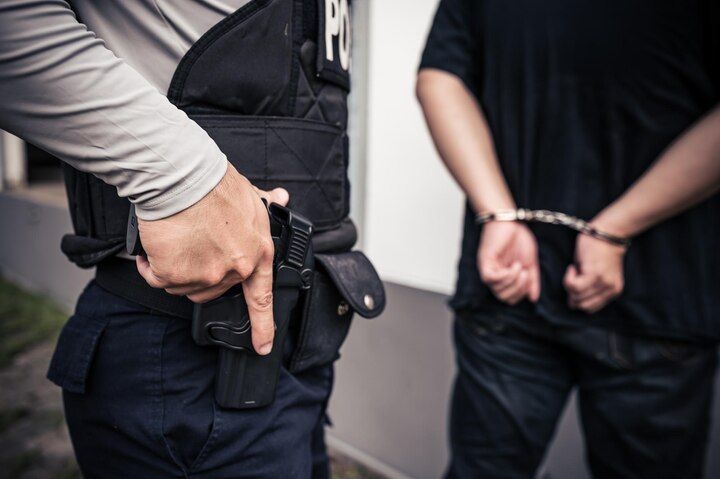 Police officer with a hand on a holstered handgun; person in handcuffs faces away. Voluntary Manslaughter Law Attorney in Nashville, Tennessee