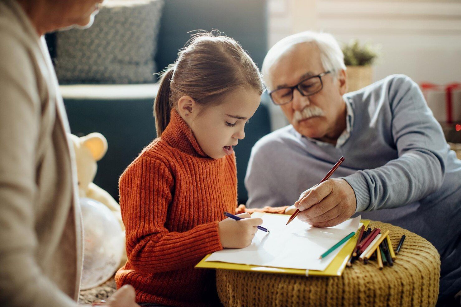 Girl and grandfather draw together, orange sweater, sitting on floor, colored pencils. Grandparent’s Rights Law Attorney in Nashville, Tennessee