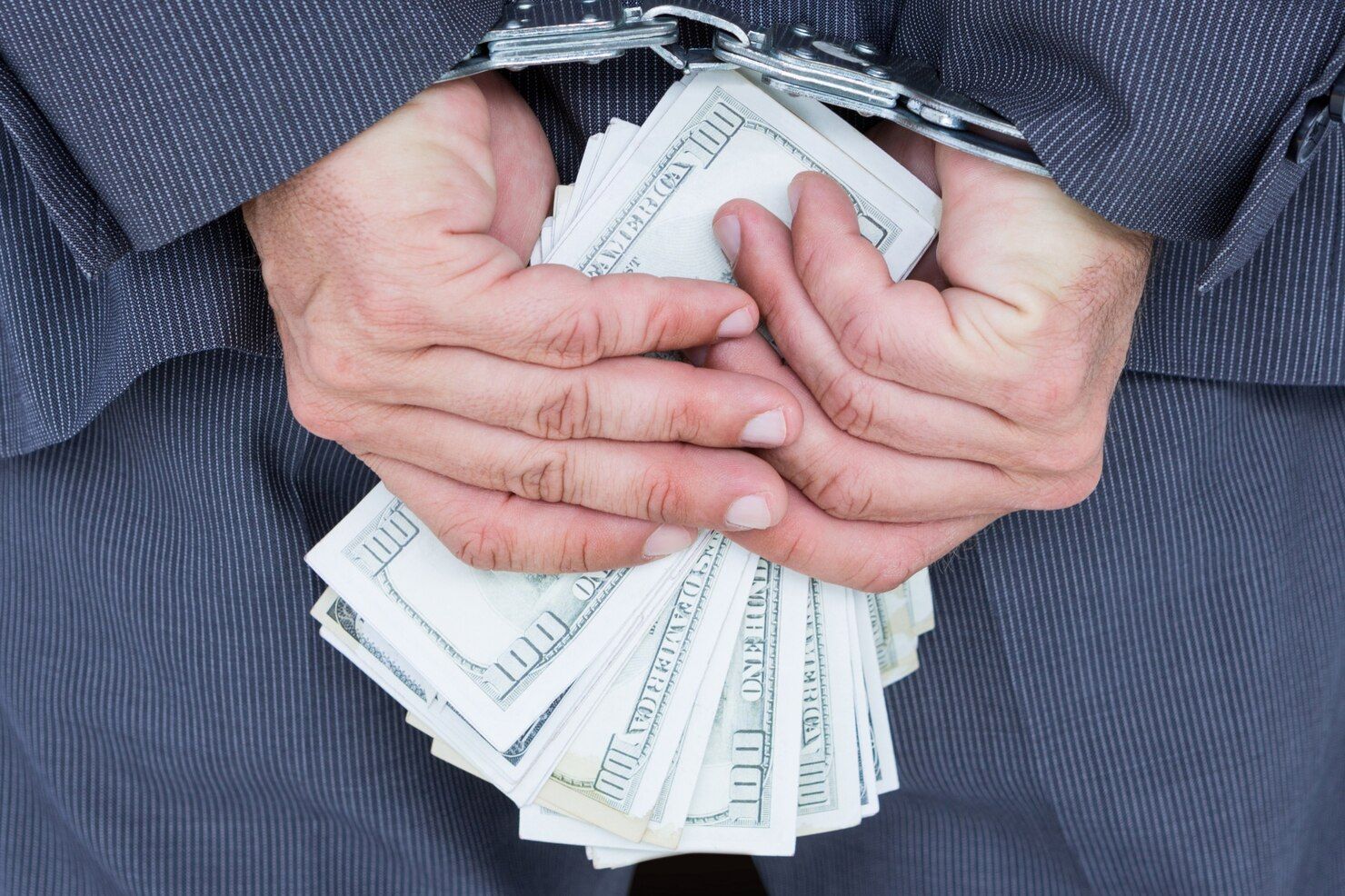 Person in suit, handcuffed behind their back, holding a large stack of US dollar bills. Money Laundering Law Attorney in Nashville, Tennessee