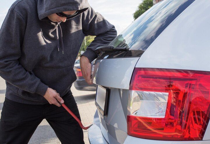 Person in hoodie prying open a car's trunk with a crowbar, outdoors. Carjacking Law Attorney in Nashville, Tennessee