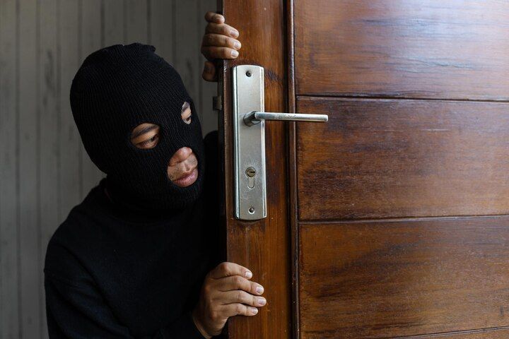 Person in black mask peeking around a wooden door. Burglary Law Attorney in Nashville, Tennessee