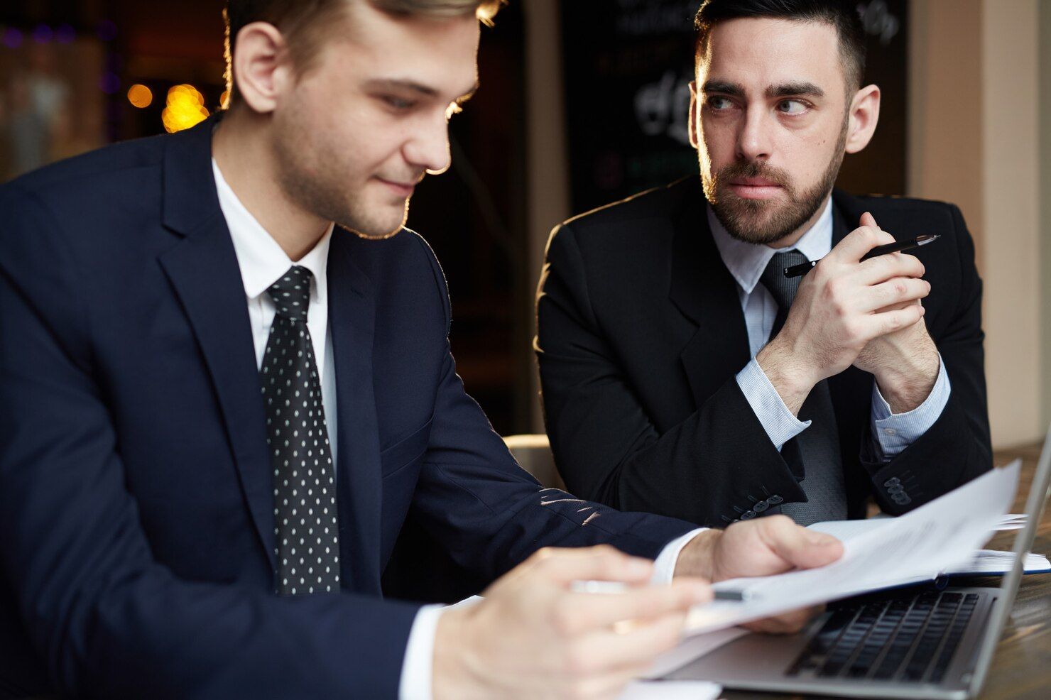 Two men in suits reviewing documents near a laptop; one points while the other looks on thoughtfully. Forgery Law Attorney in Nashville, Tennessee