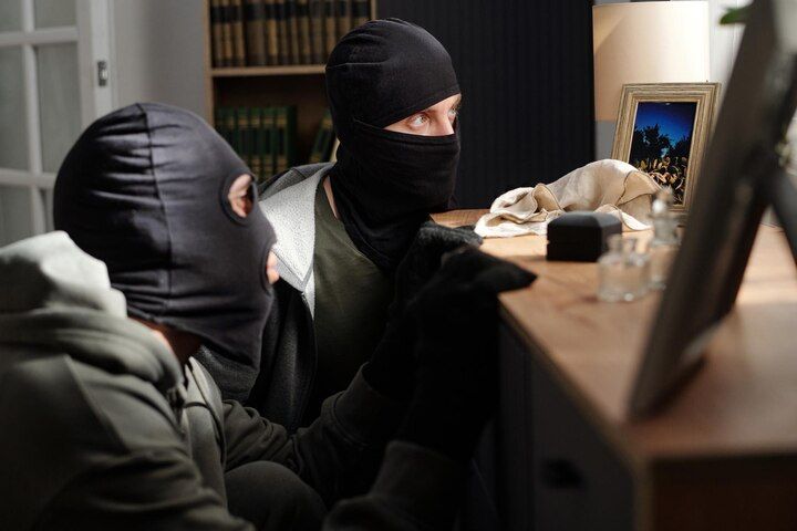 Two people wearing black ski masks examining an object on a table in a dimly lit room. Aggravated Criminal Trespass Law Attorney in Nashville, Tennessee