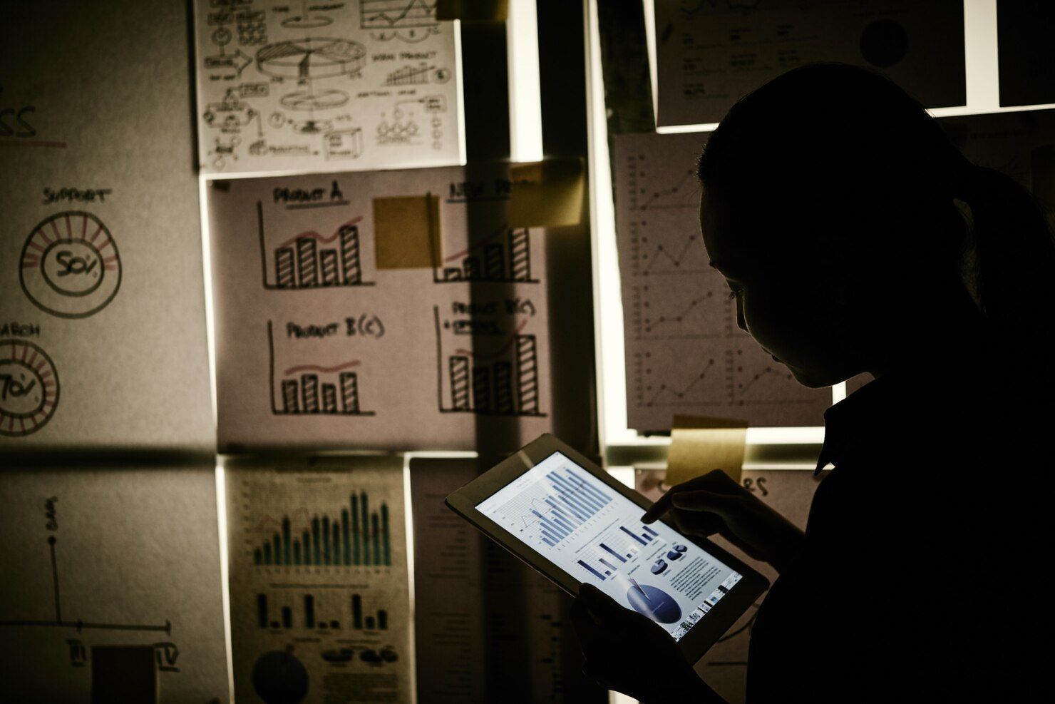 Person using a tablet, backlit by charts and diagrams pinned to a wall. Criminal Simulation Law Attorney in Nashville, Tennessee