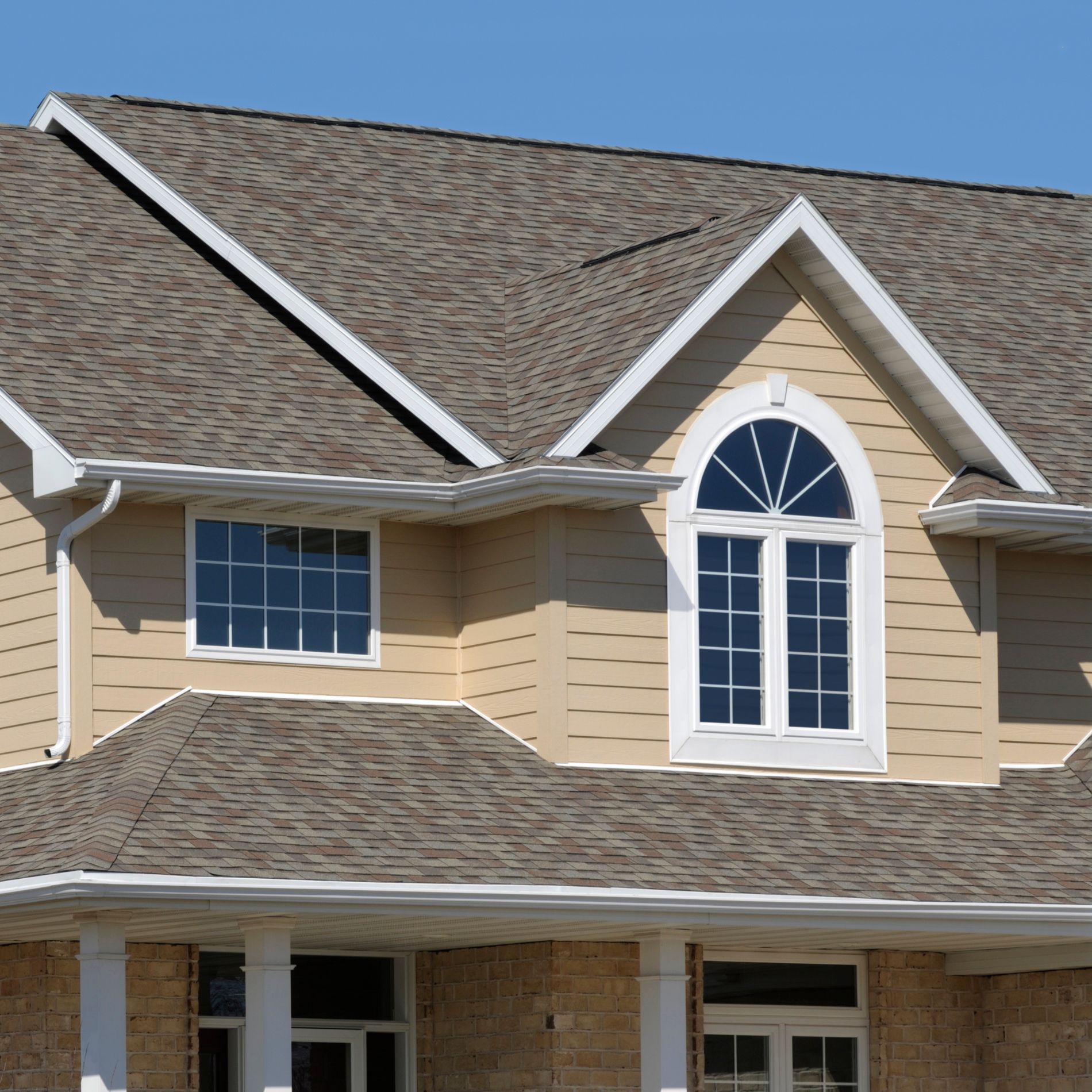 Beige house with tan siding, brown roof, white trim, and arched window.