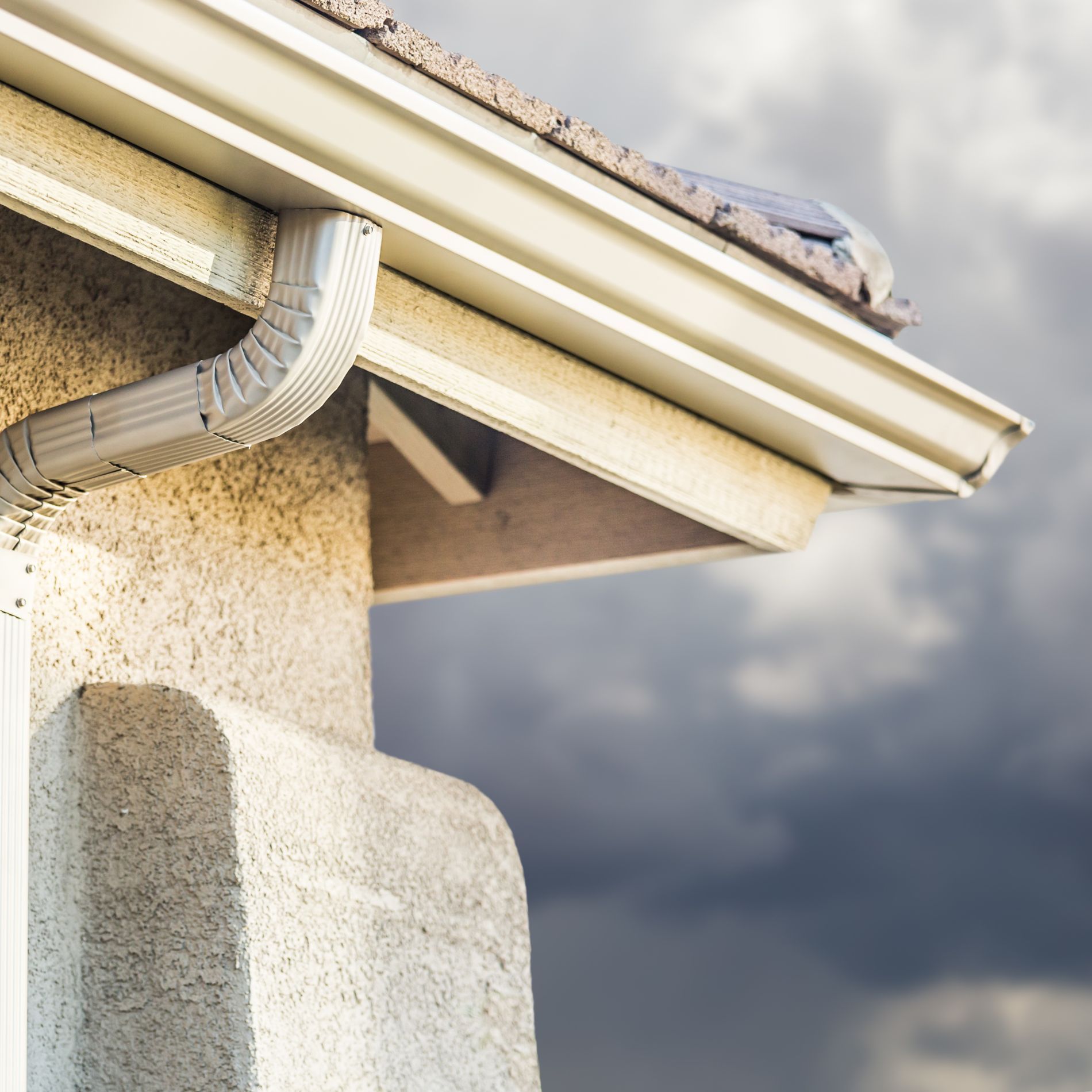 Gutter on a stucco house with a dark, cloudy sky in the background.