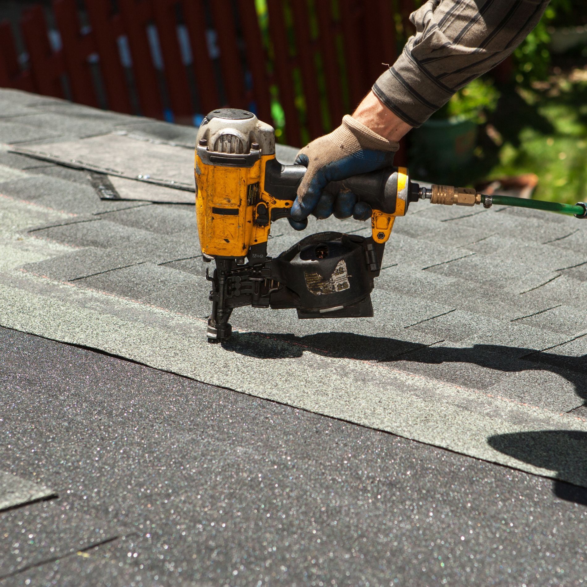 Person using a yellow nail gun to install roofing shingles.