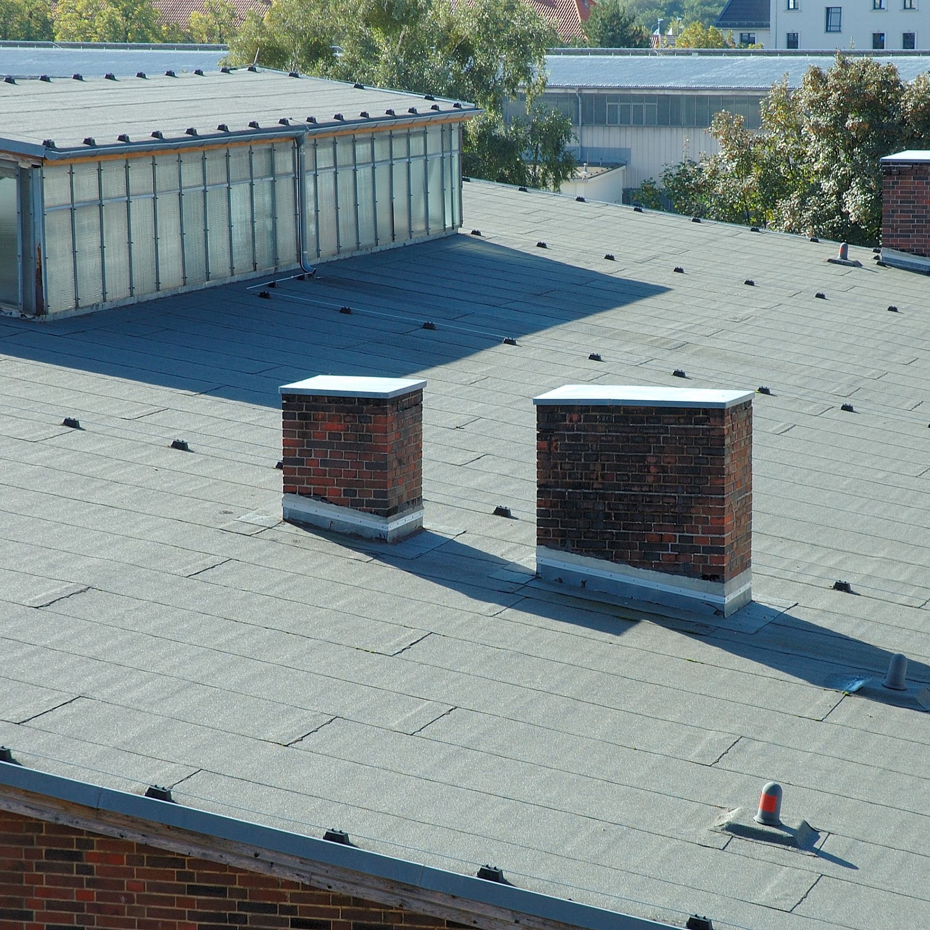 Flat roof with two brick chimneys, skylight, and fasteners.