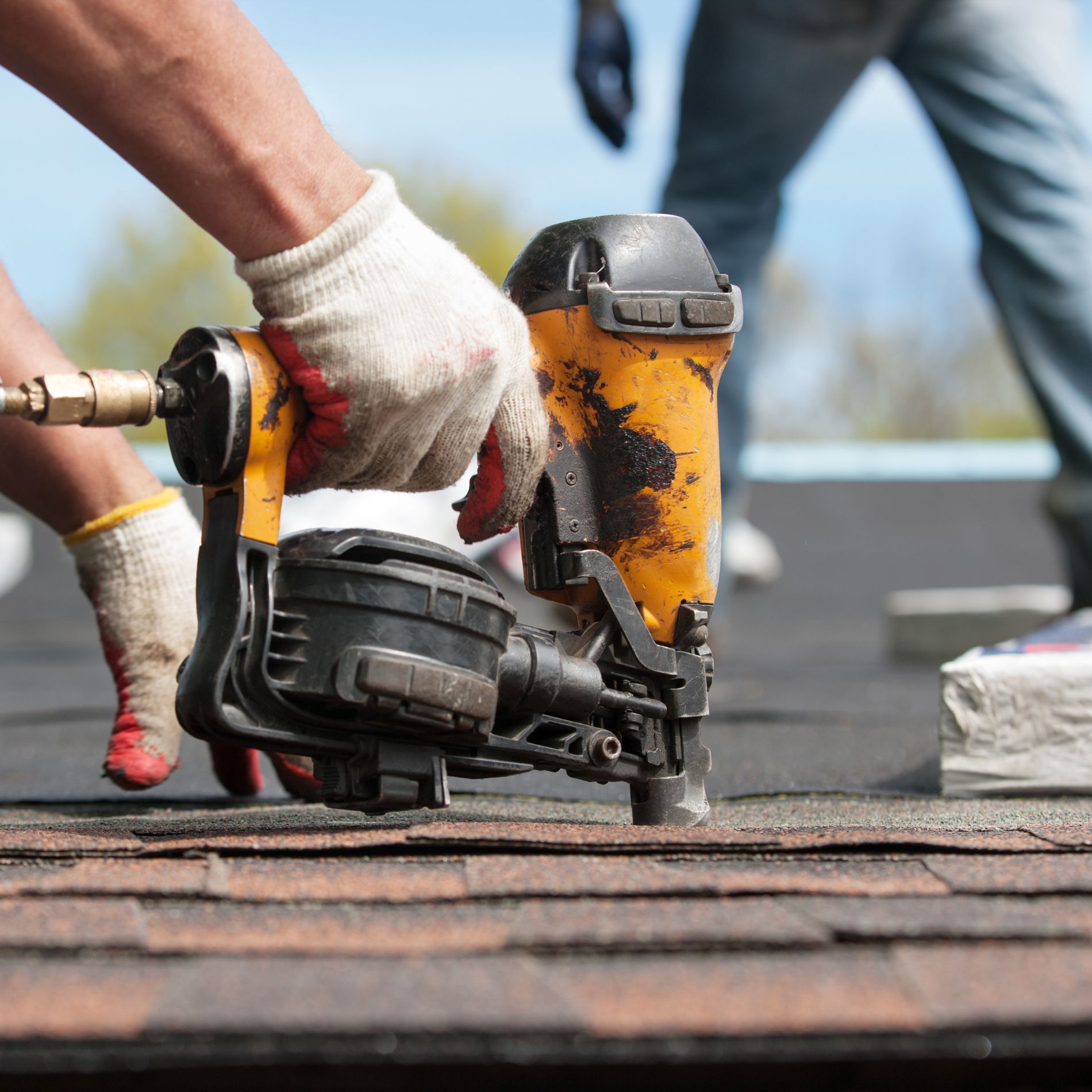 Person using a nail gun to install shingles on a roof.