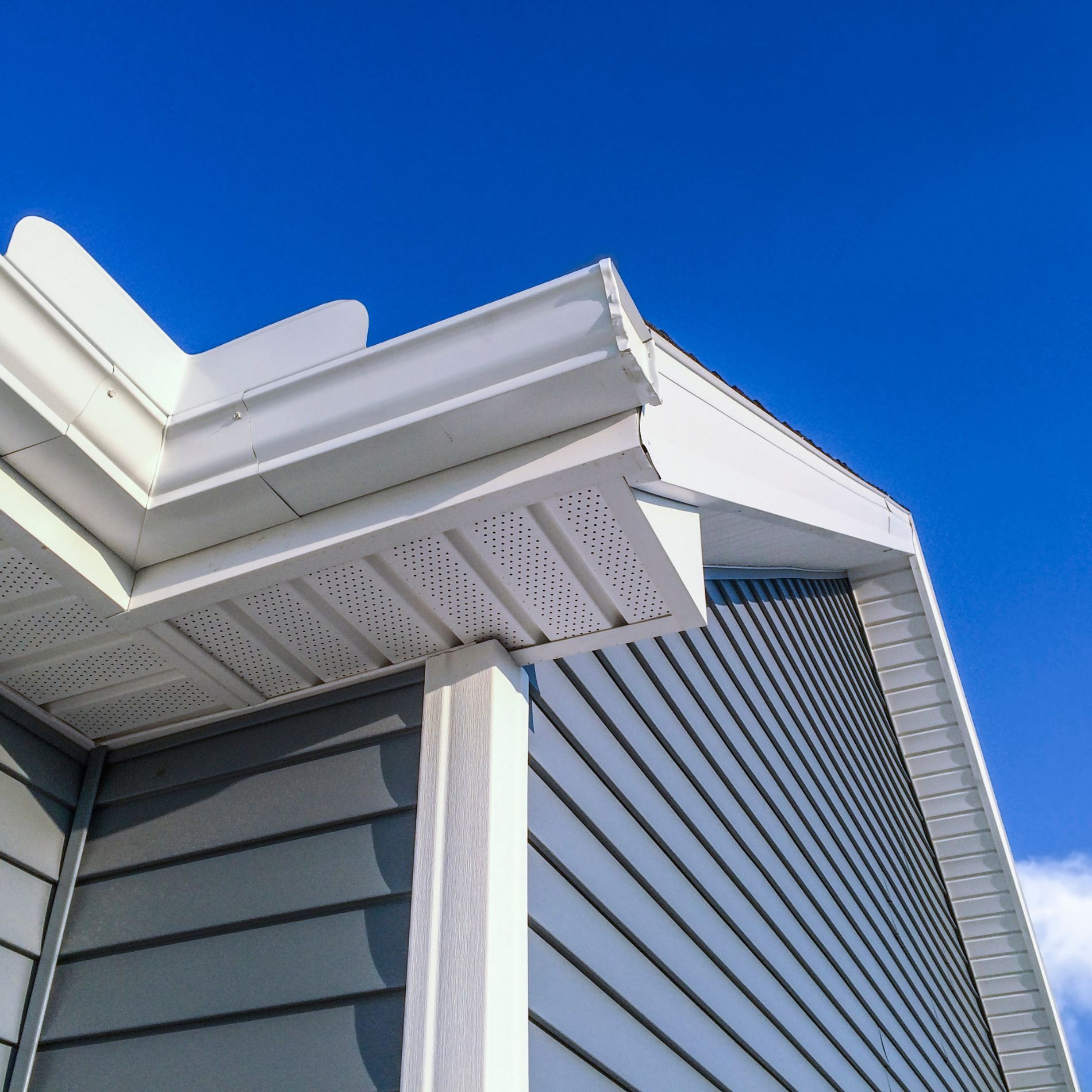 Blue siding and white trim on the corner of a house, against a bright blue sky.