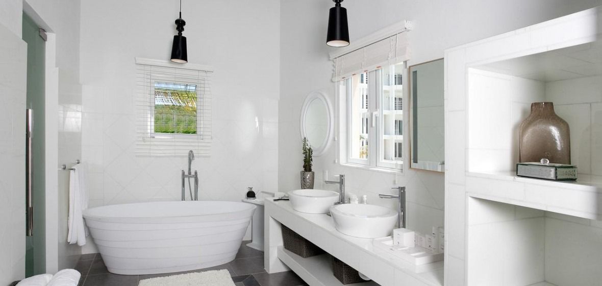 White bathroom with a tub, sinks, and shelves. A window allows natural light to enter.