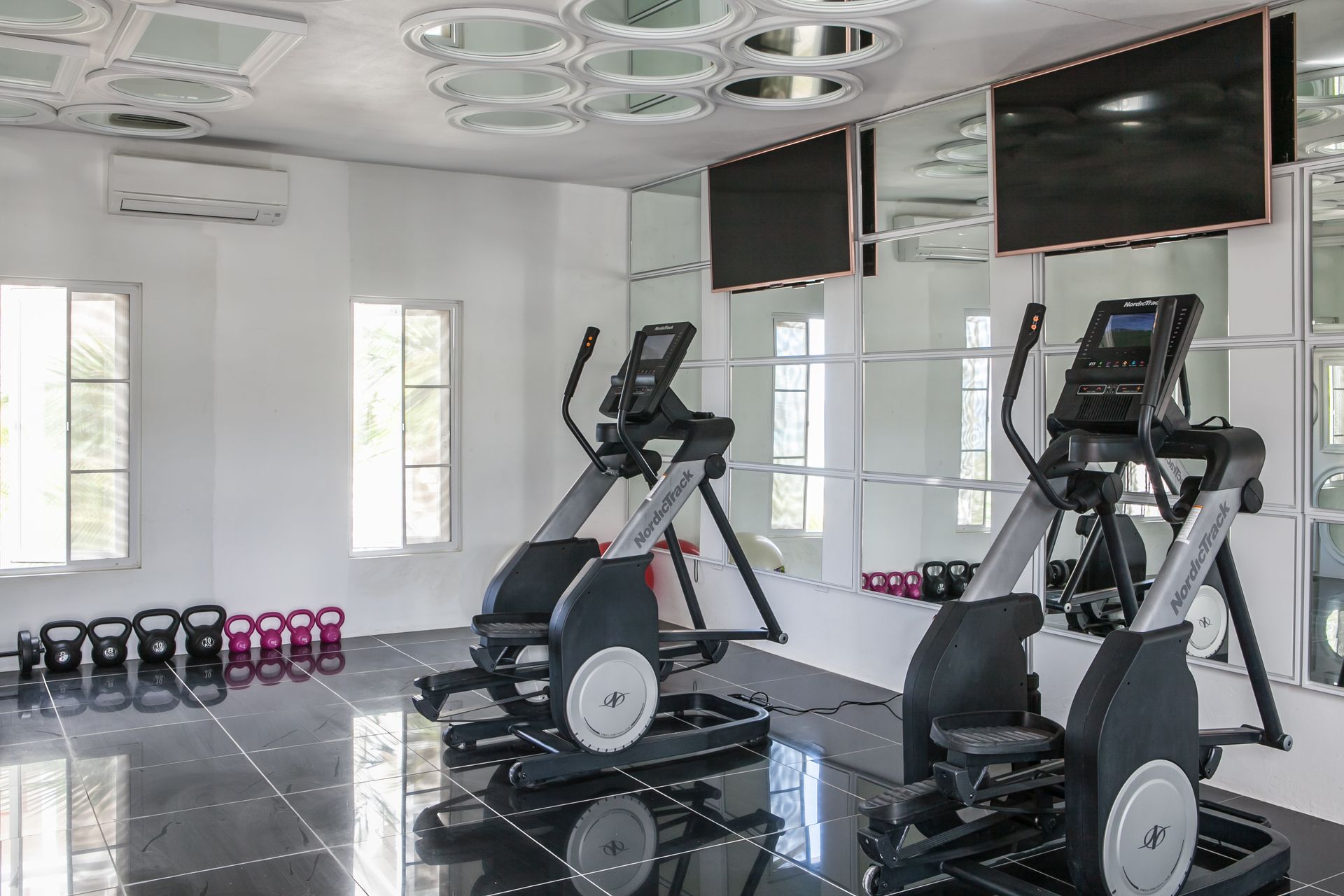 Gym interior with elliptical machines, weights, and mirrors; a bright, clean space.