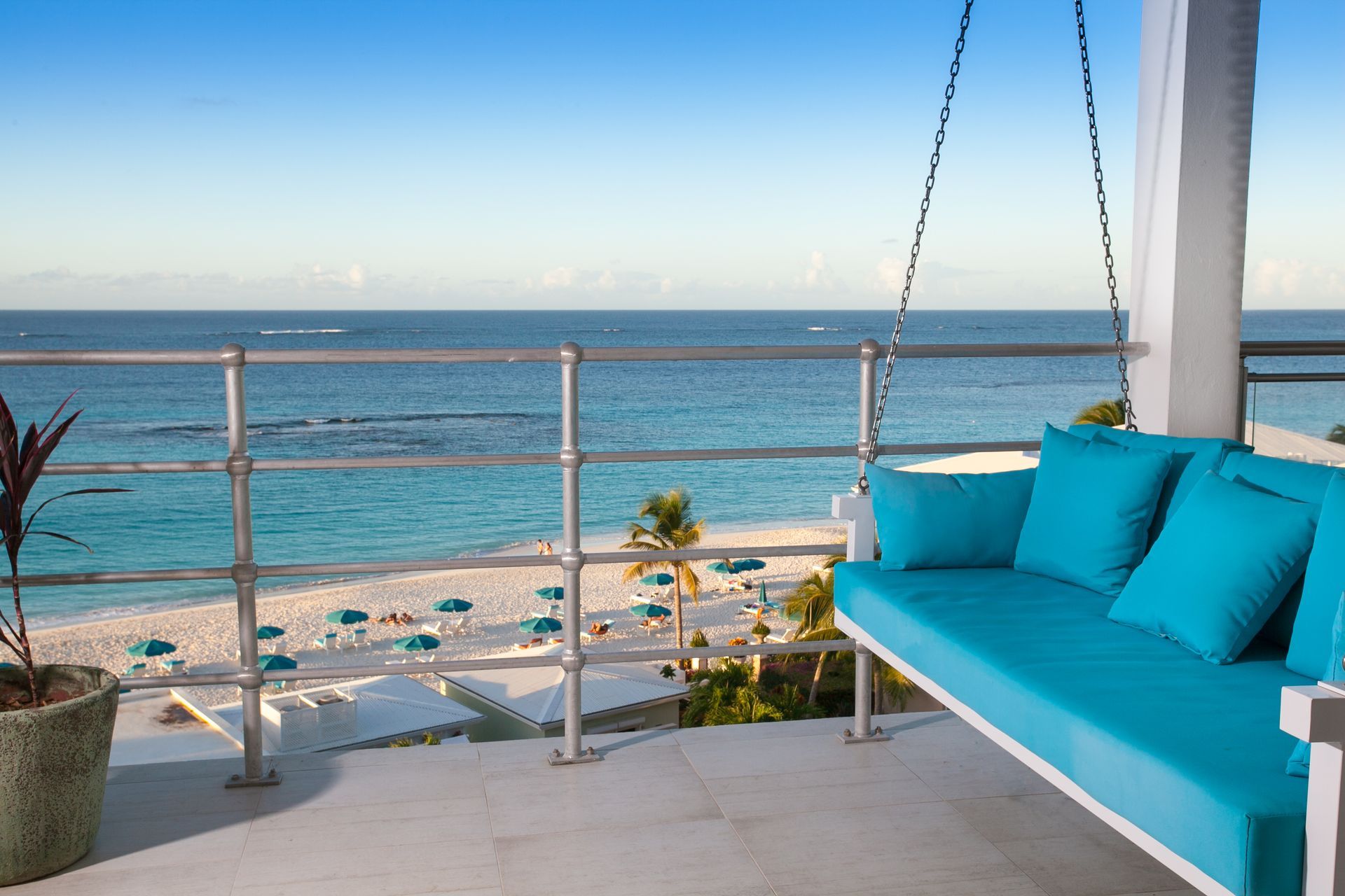 Balcony with turquoise swing overlooking a white sand beach and ocean.