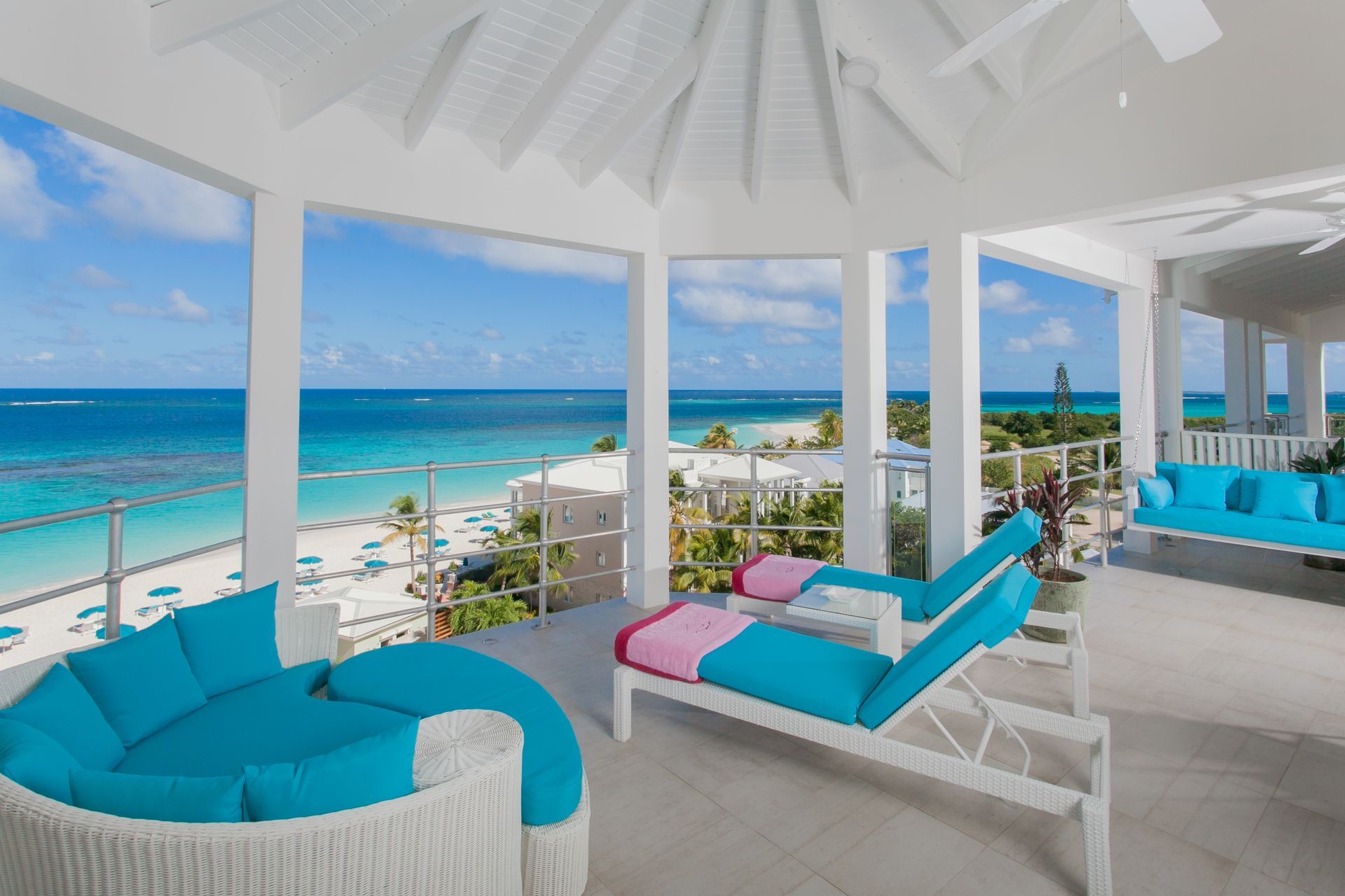 Balcony overlooking a beach with turquoise lounge furniture and ocean view.