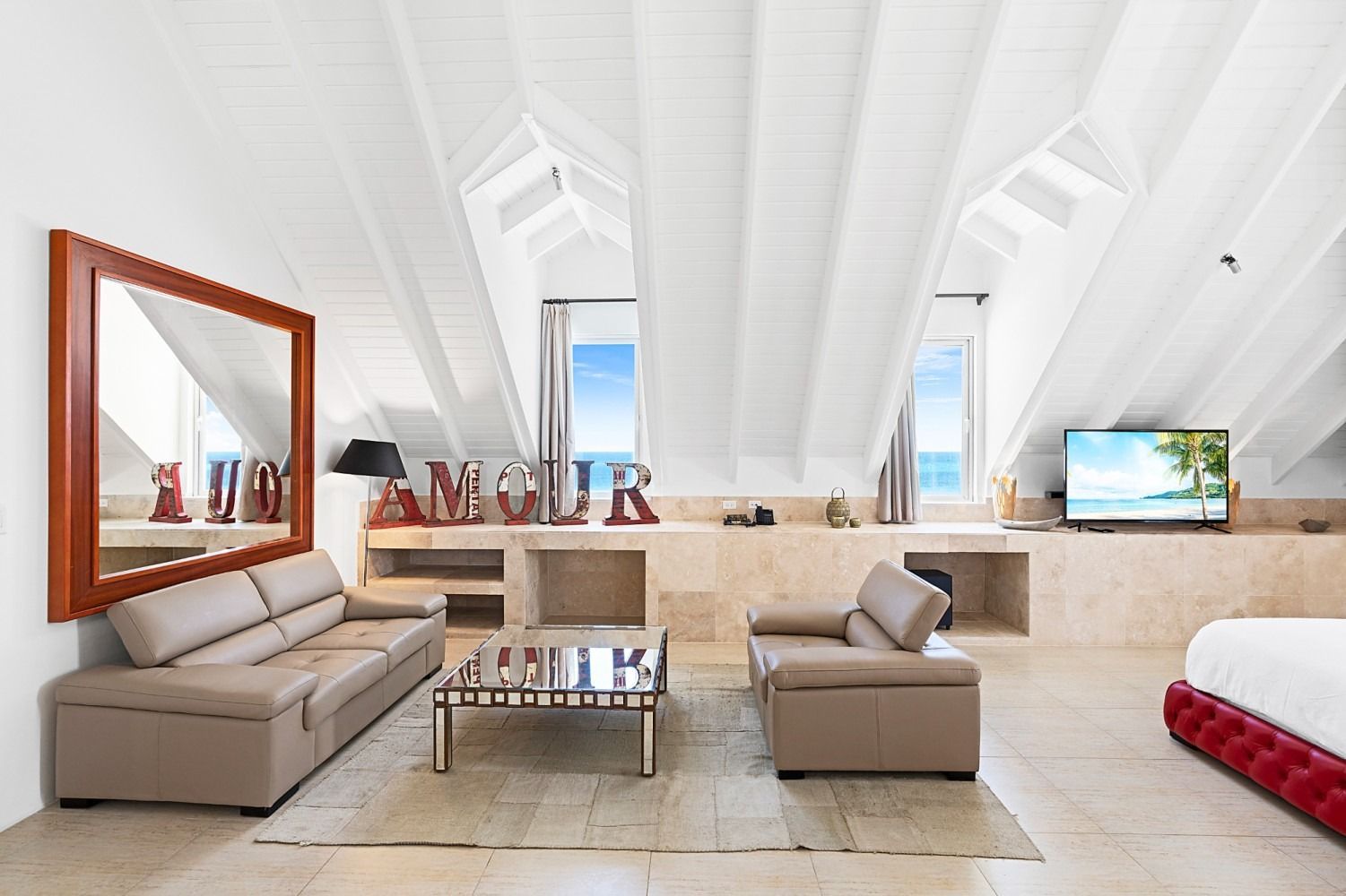 Spacious, bright living room with high, white-beamed ceiling, beige sofa, ocean view windows.