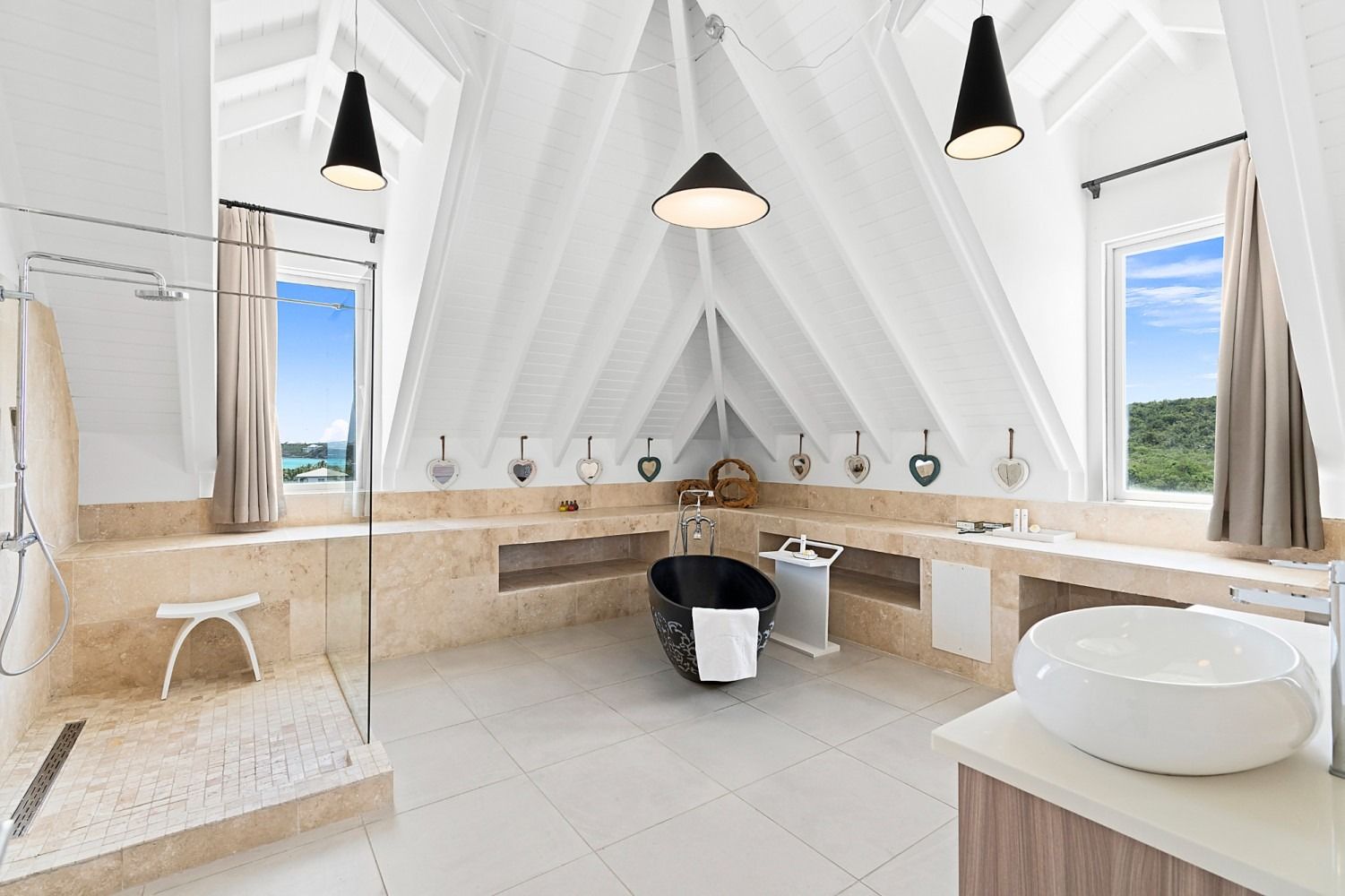 Spacious bathroom with vaulted ceiling, black bathtub, stone walls, and large windows.