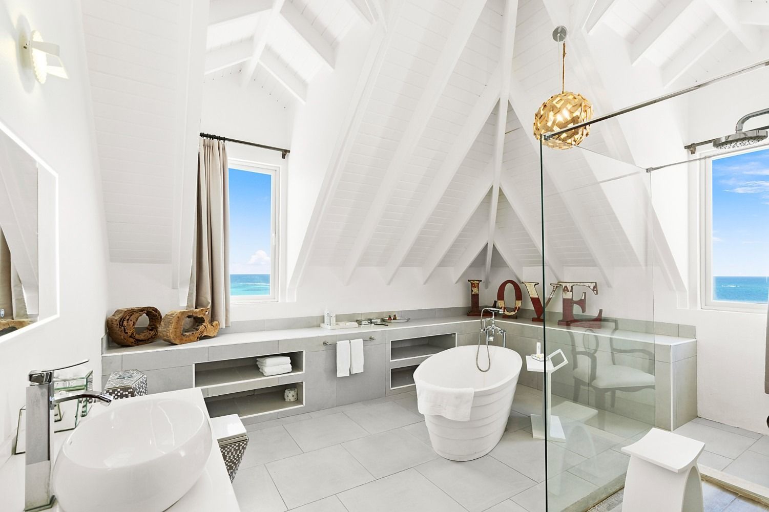 White bathroom with vaulted ceiling, soaking tub, and ocean view.