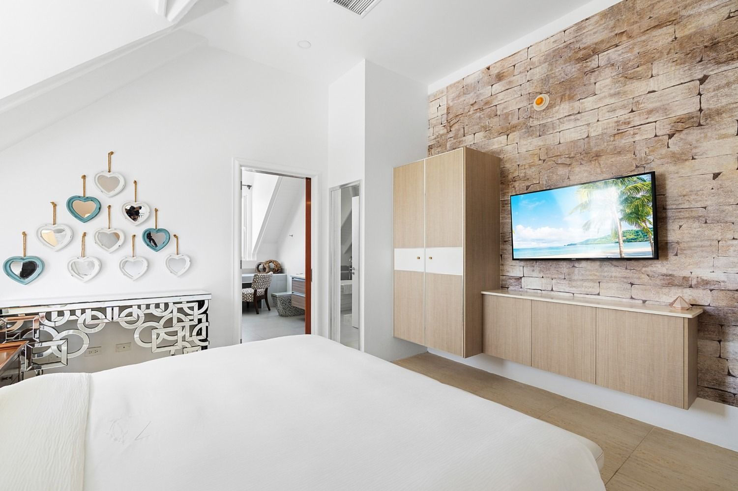 Bedroom with white bedding, exposed brick wall, wooden cabinets, and a mounted TV.