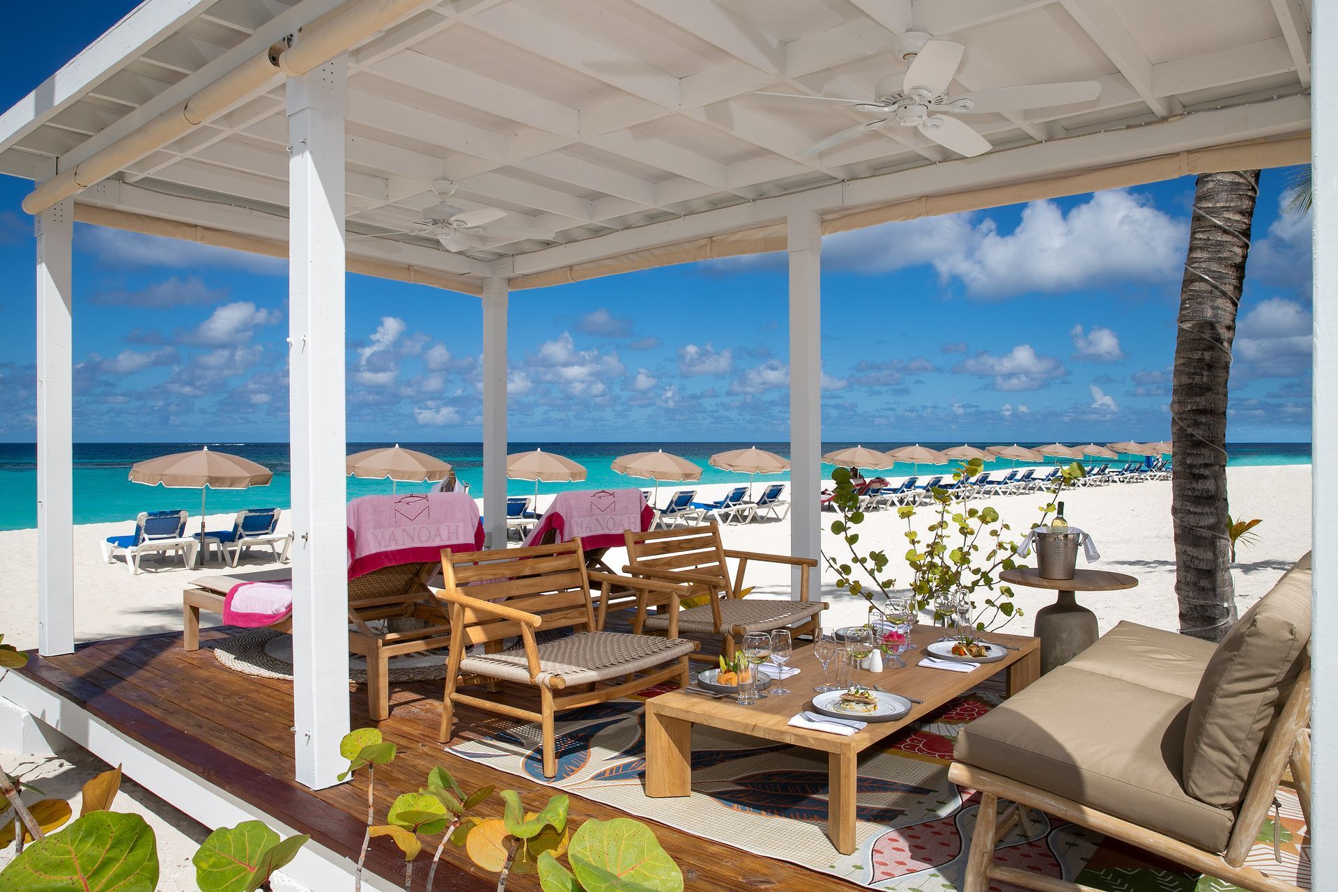 Beachfront patio with wooden lounge furniture, white canopy, and turquoise ocean view