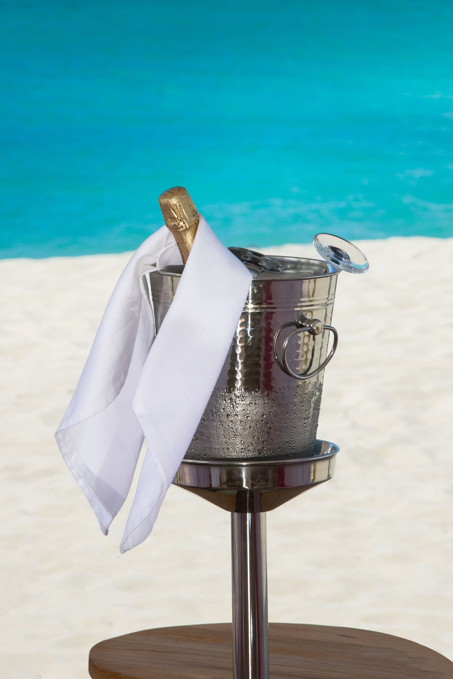 A silver bucket with white towels on a stand against a beach and ocean backdrop.