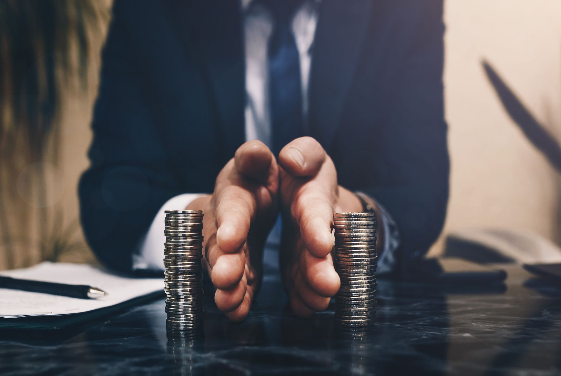 Hands pressing together beside stacked coins on a desk, suggesting saving or financial stress