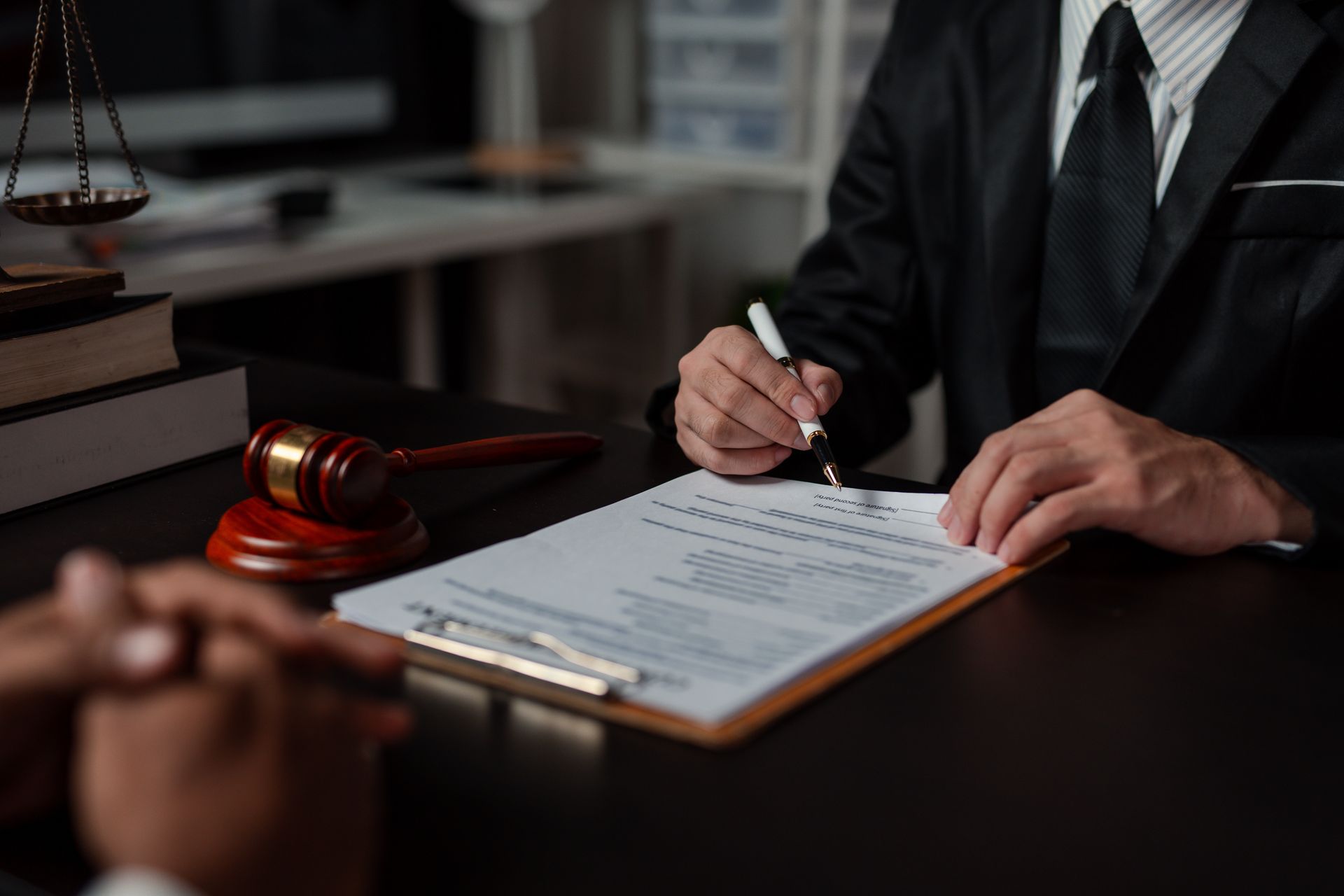 Lawyer signing a document at a desk beside a judge’s gavel in a courtroom setting