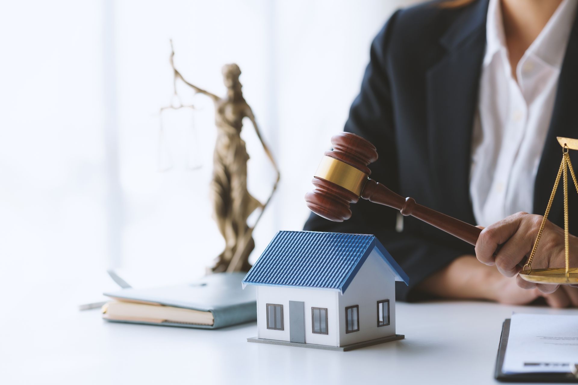 Lawyer holding gavel beside scales and a model house on a desk