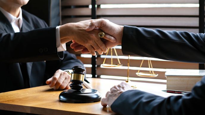Two suited people shaking hands over a gavel in a law office