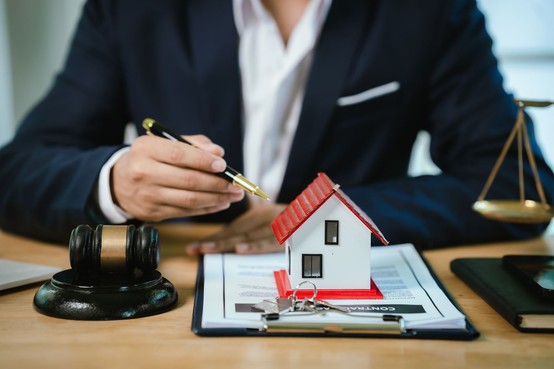 Lawyer reviewing a house model on contract papers with a gavel and scales of justice