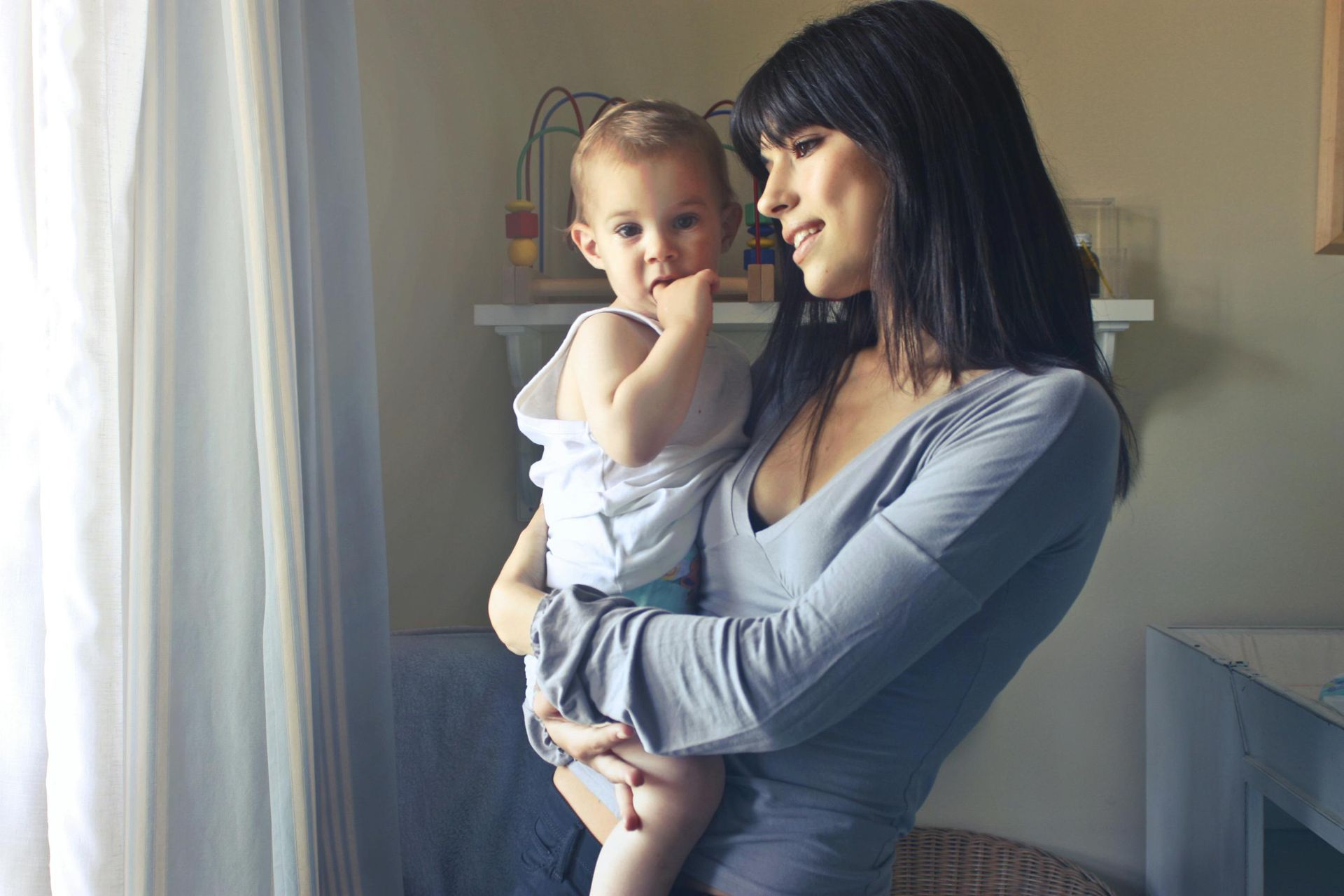 A woman is holding a baby in her arms in front of a window.