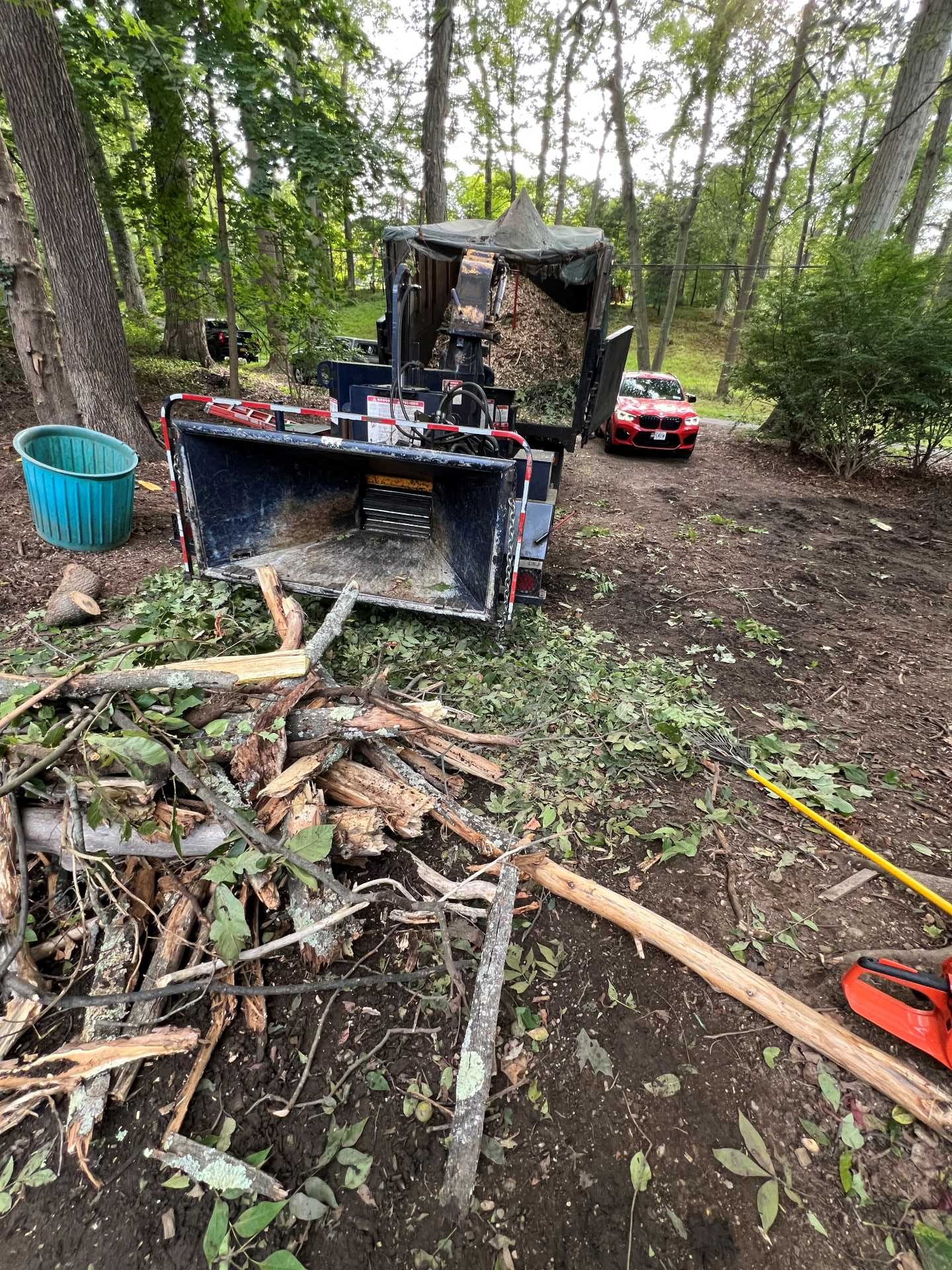 A wood chipper processes branches on a wooded lot; a car and bucket are visible nearby.