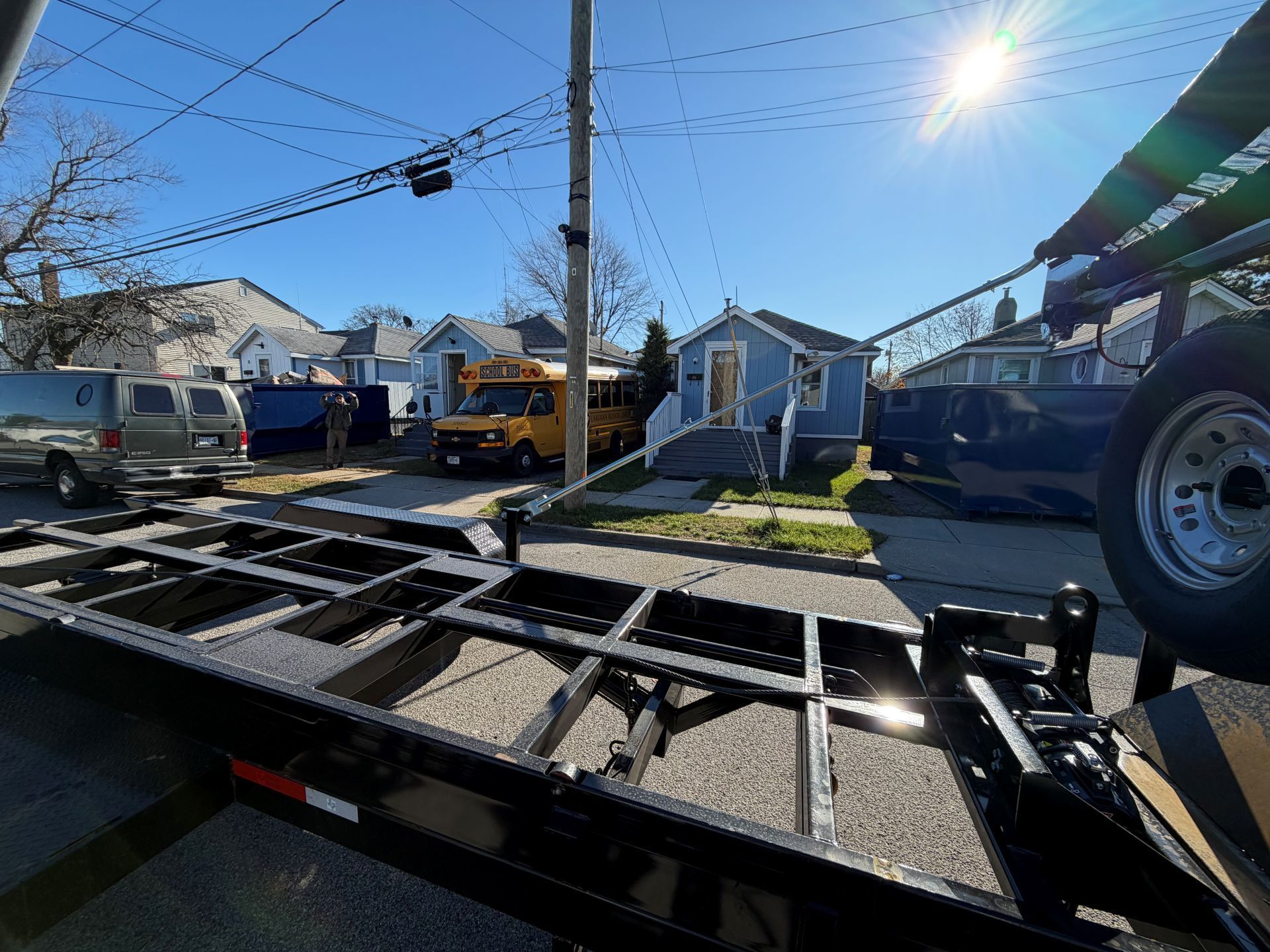 Empty trailer with a school bus, houses, and utility pole on a sunny day.