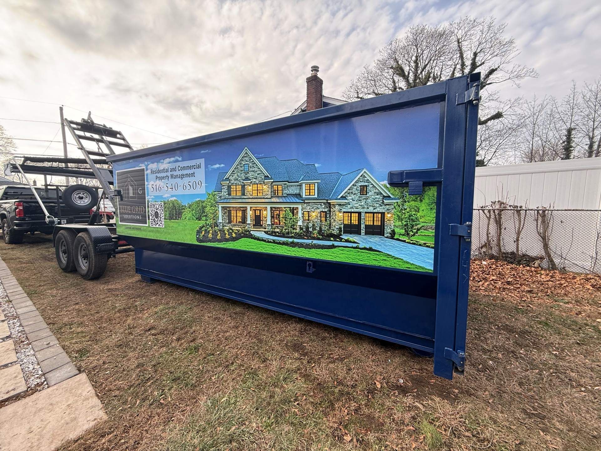 A blue container with a house graphic on a trailer in front of a house.