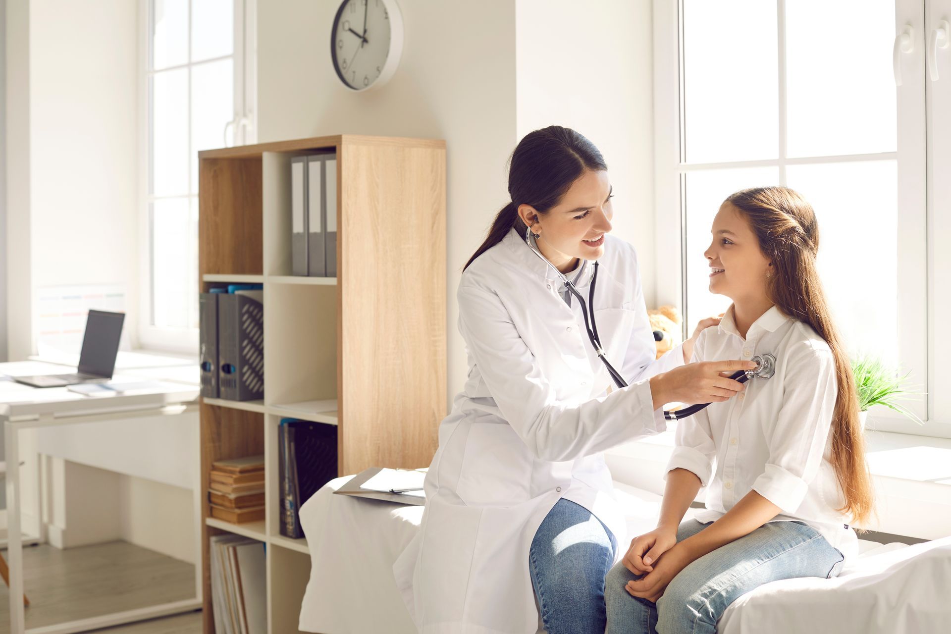 Doctor using a stethoscope to examine a patient. They are in a well-lit medical exam room.