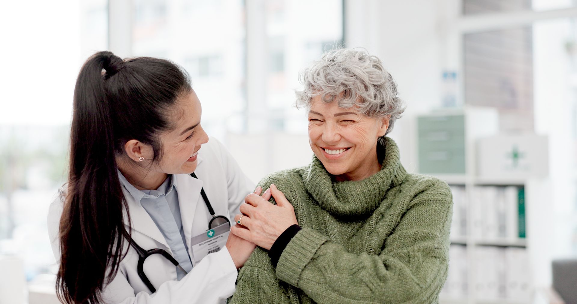 Doctor comforts patient, placing hand on shoulder; both smile, likely in a medical office.