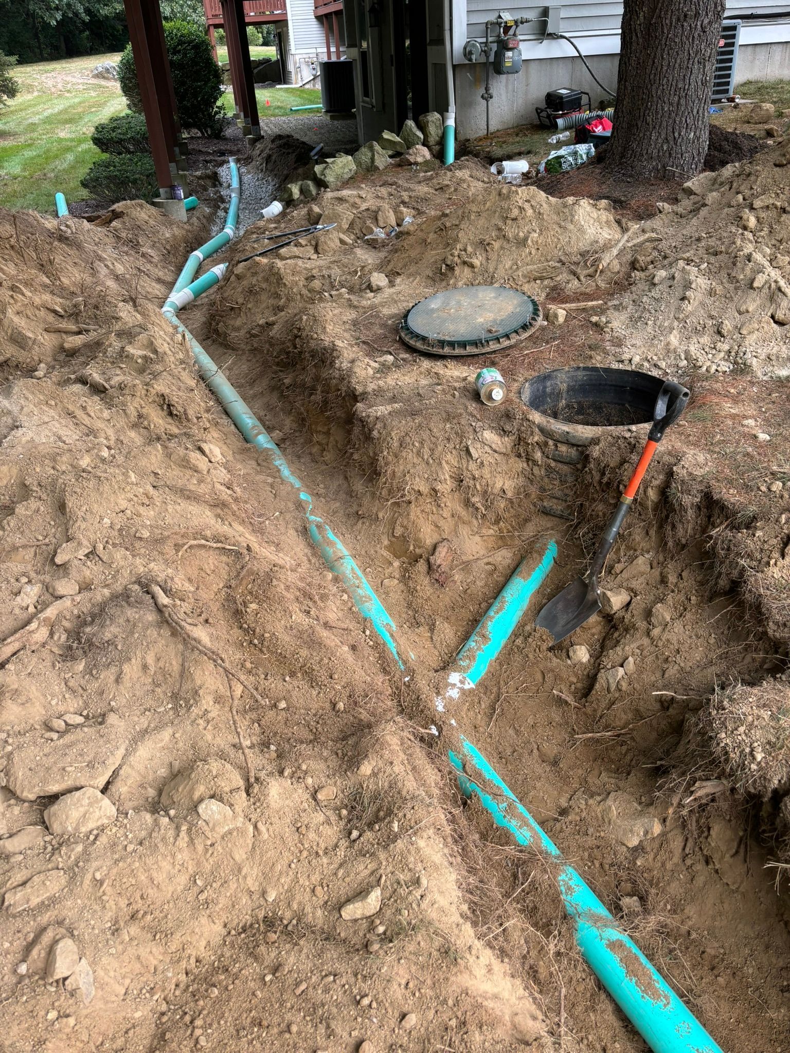 Trenched dirt yard with turquoise pipe, utility access covers, and a black pipe emerging from the ground
