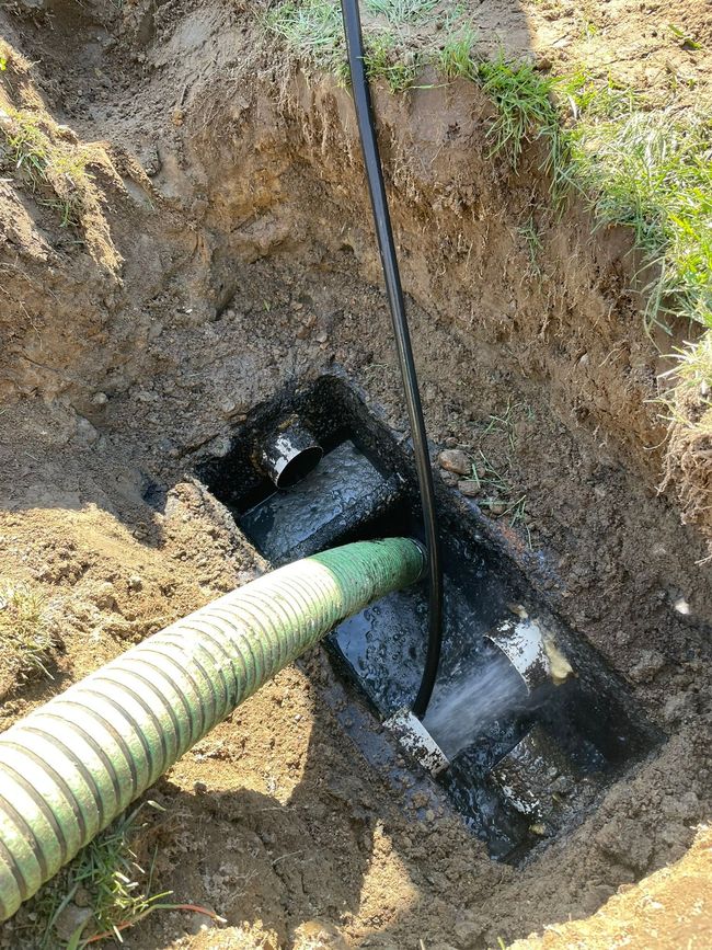 Worker in a trench using an orange jackhammer beside a building during excavation work