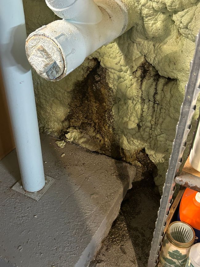 Insulated pipes and foam-covered wall with a rough floor opening in a basement corner