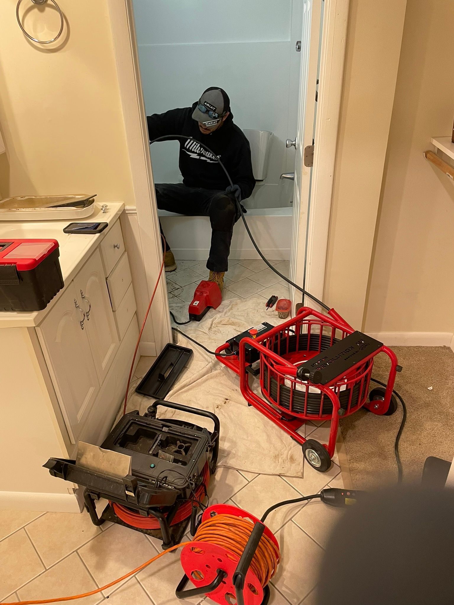 Person in a bathroom near several red and black tools, with debris scattered on the floor.
