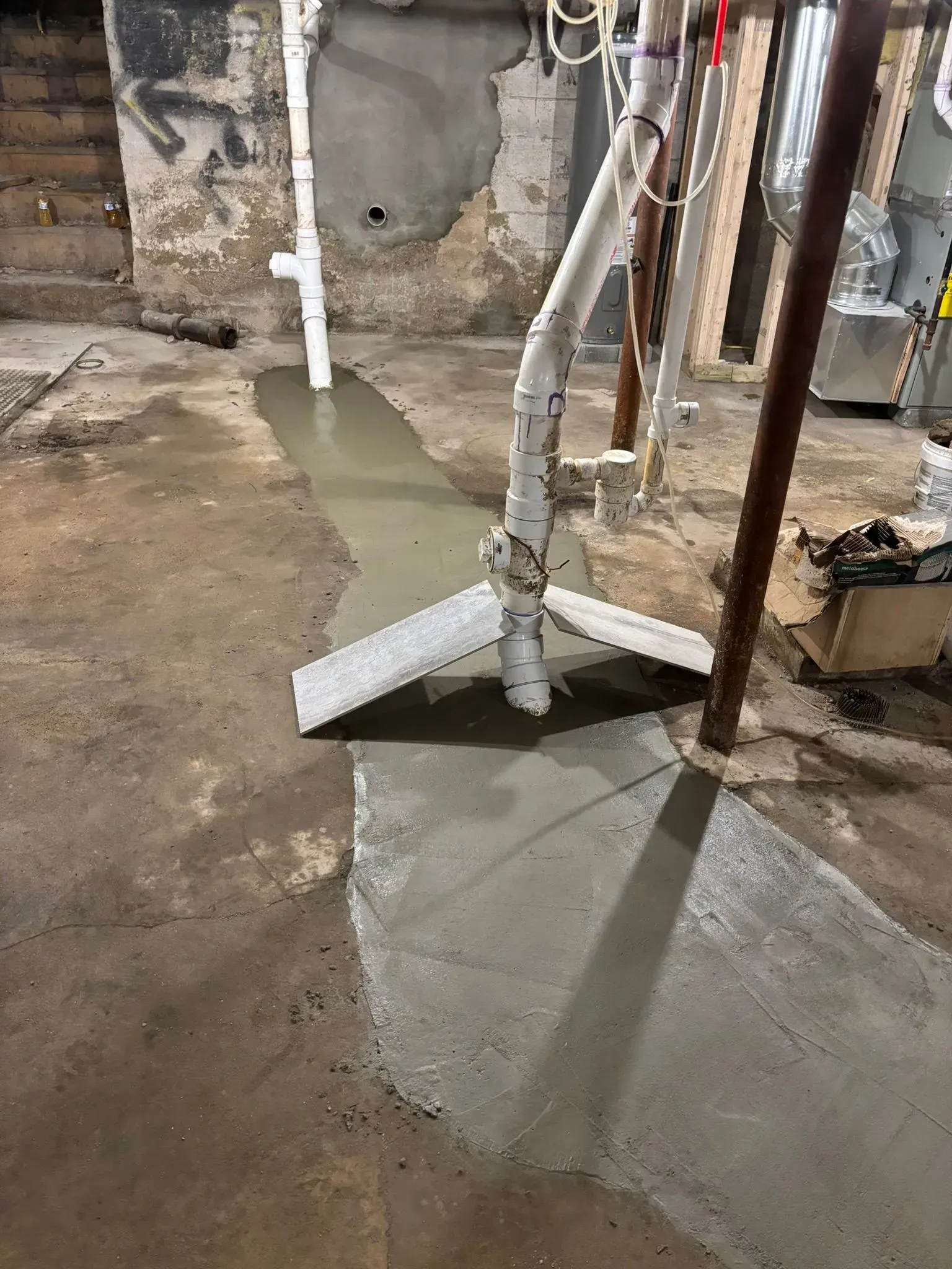 Concrete being poured around a pipe in a basement work area.