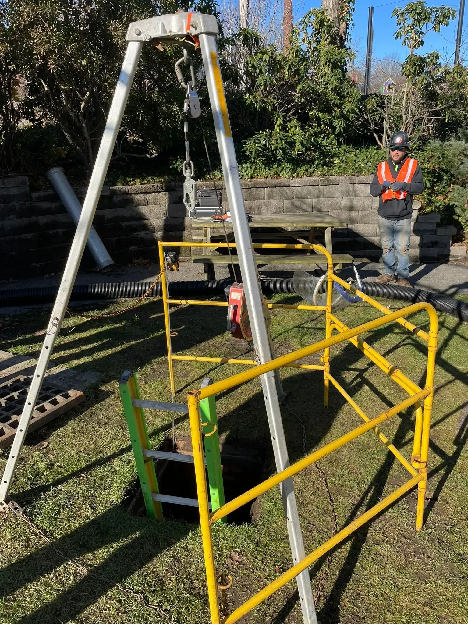 Worker in orange vest near a metal inspection rig and yellow safety barriers outdoors by railway tracks